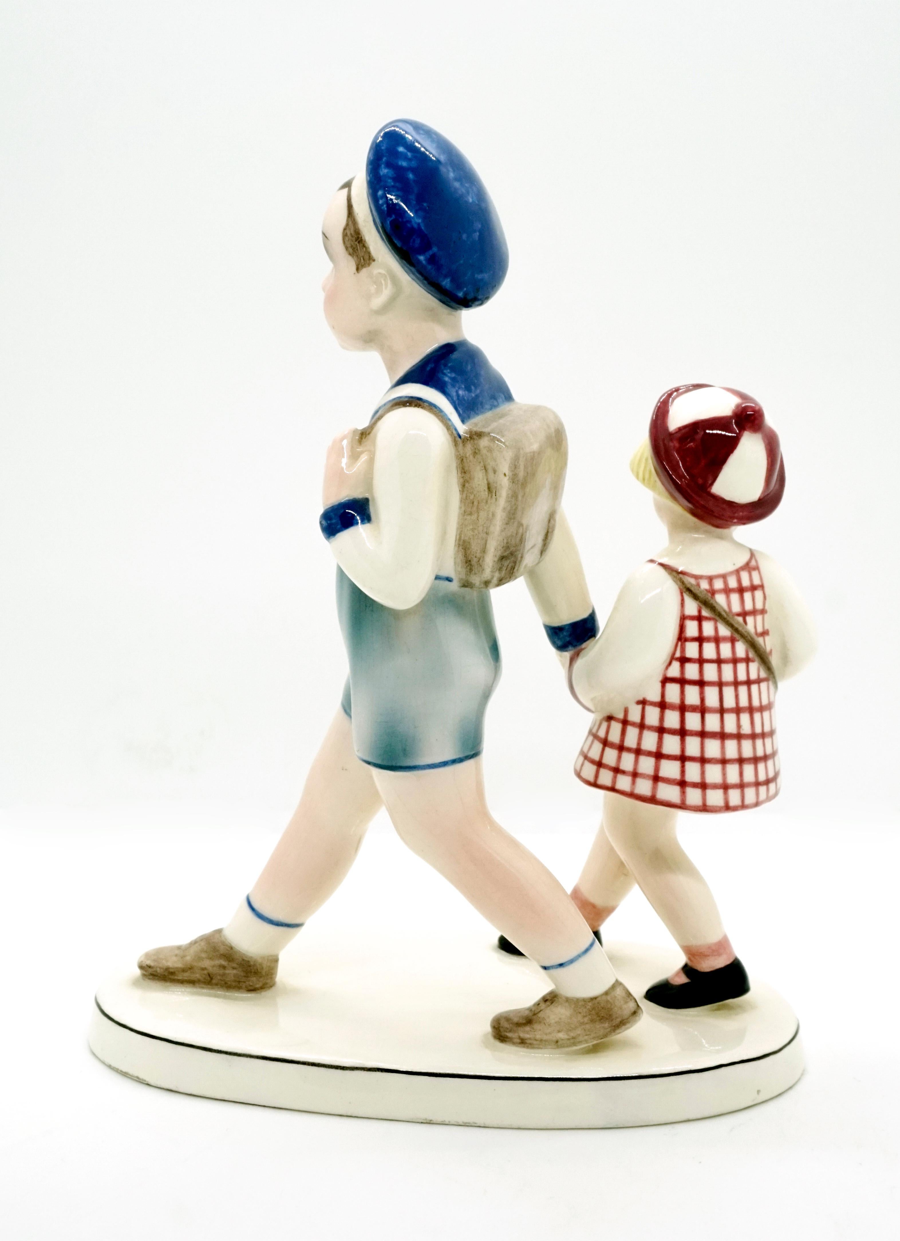 Especially rare goldscheider ceramic figurine group.
Boy in sailor suit with shorts, long-sleeved top and sailor hat, carrying a school bag on his back, leading a smaller girl lost in thought, clad in a short, plaid dress and red and white hat, by