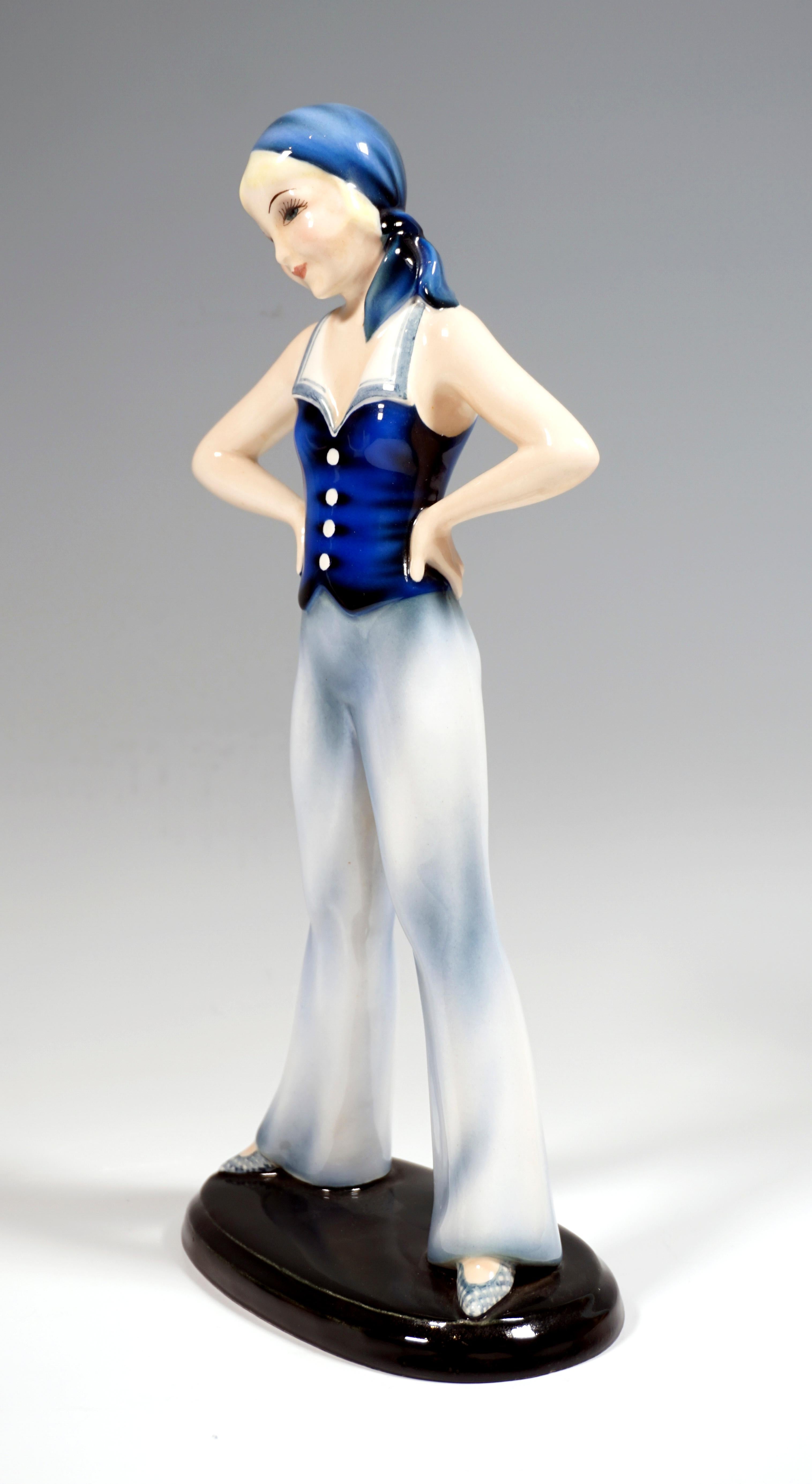 Très rare figurine en céramique Art Déco de Goldscheider.
Jeune fille aux cheveux blonds attachés et au foulard bleu noué dans le dos, vêtue d'une blouse bleue sans manches à col marin et d'un large pantalon à cloche bleu clair, debout, les jambes