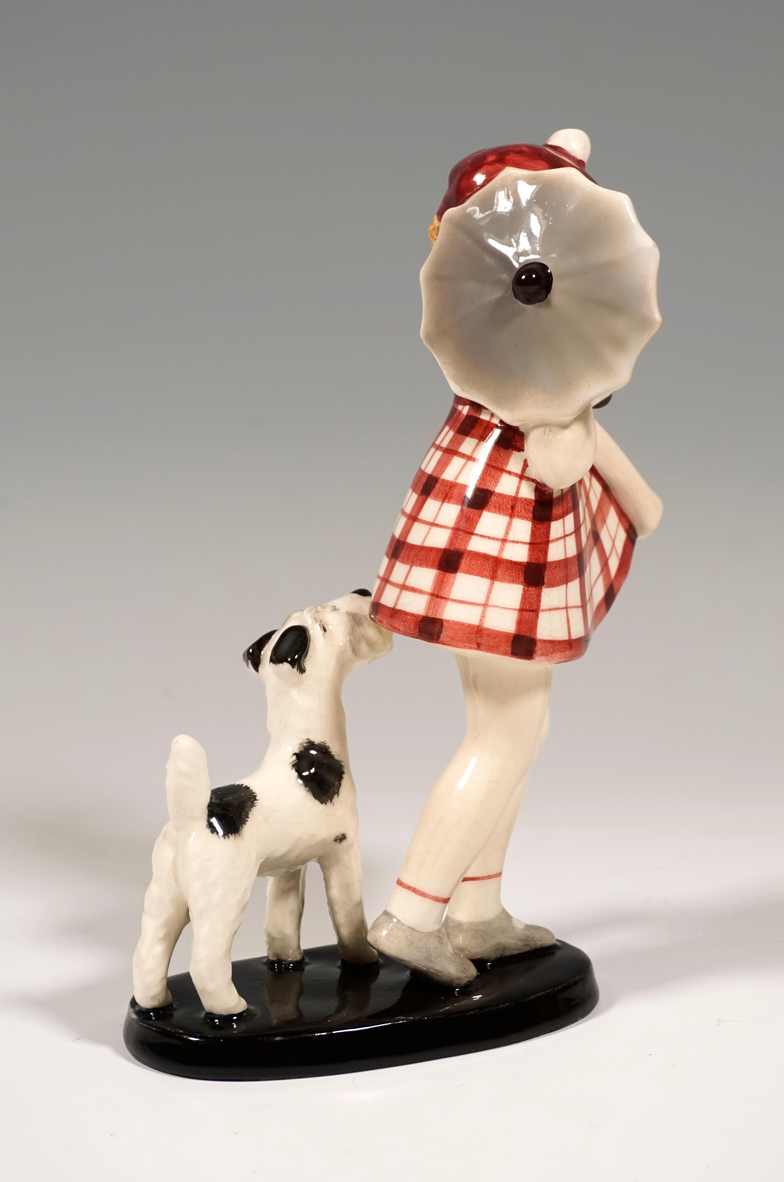 Rare Goldscheider ceramic figurine group of the 1030s:
Little girl in a red checkered dress and with a red cap, holding a small umbrella on her shoulder, anxiously looking over her other shoulder at a small fox terrier behind her.
On a black, oval