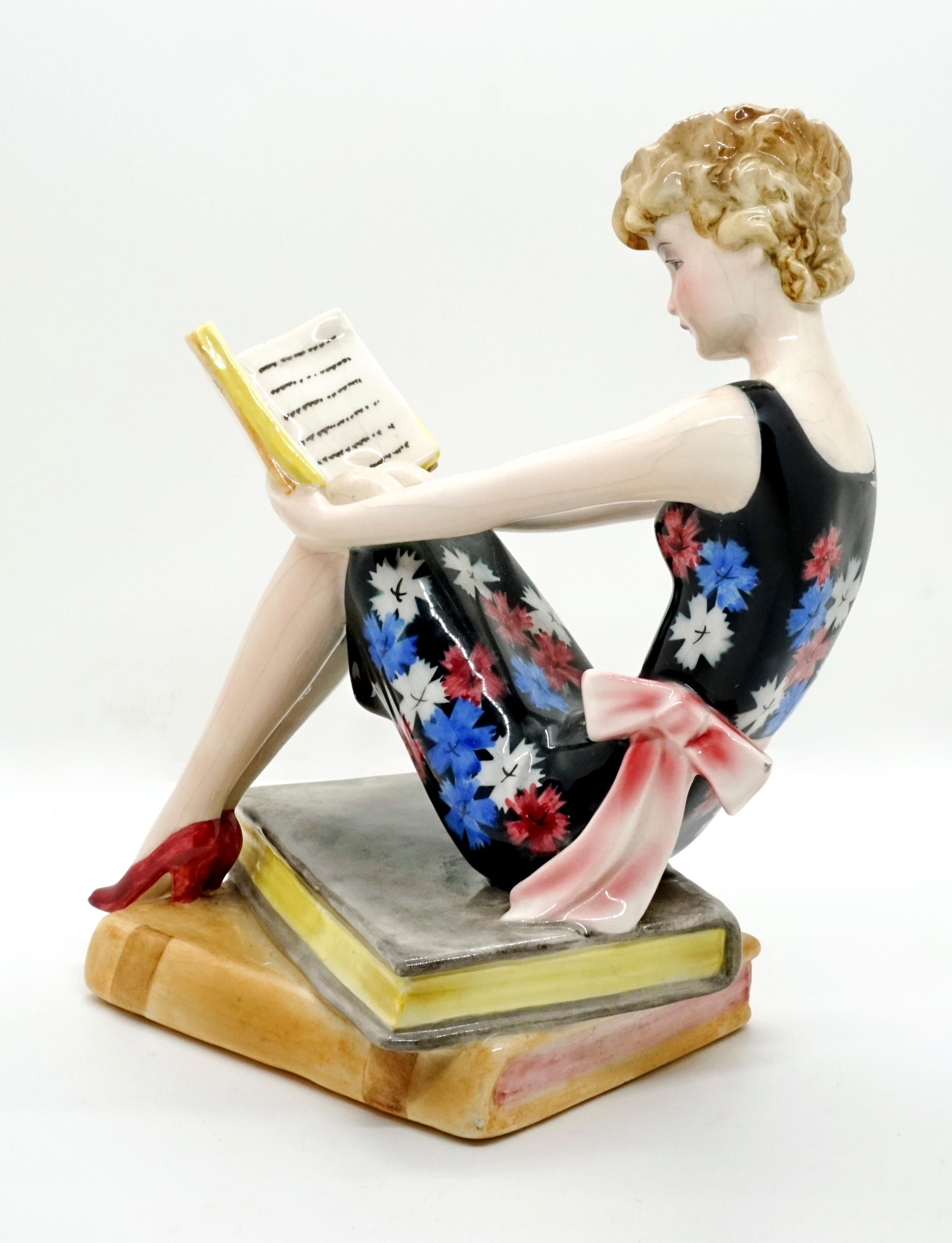Very rare goldscheider Art Deco ceramic figurine.
A young lady with blond curly hair, a flowered summer dress and a large bow around her waist, is sitting on a pile of large books that also serves as a pedestal, reading a book, which she is holding