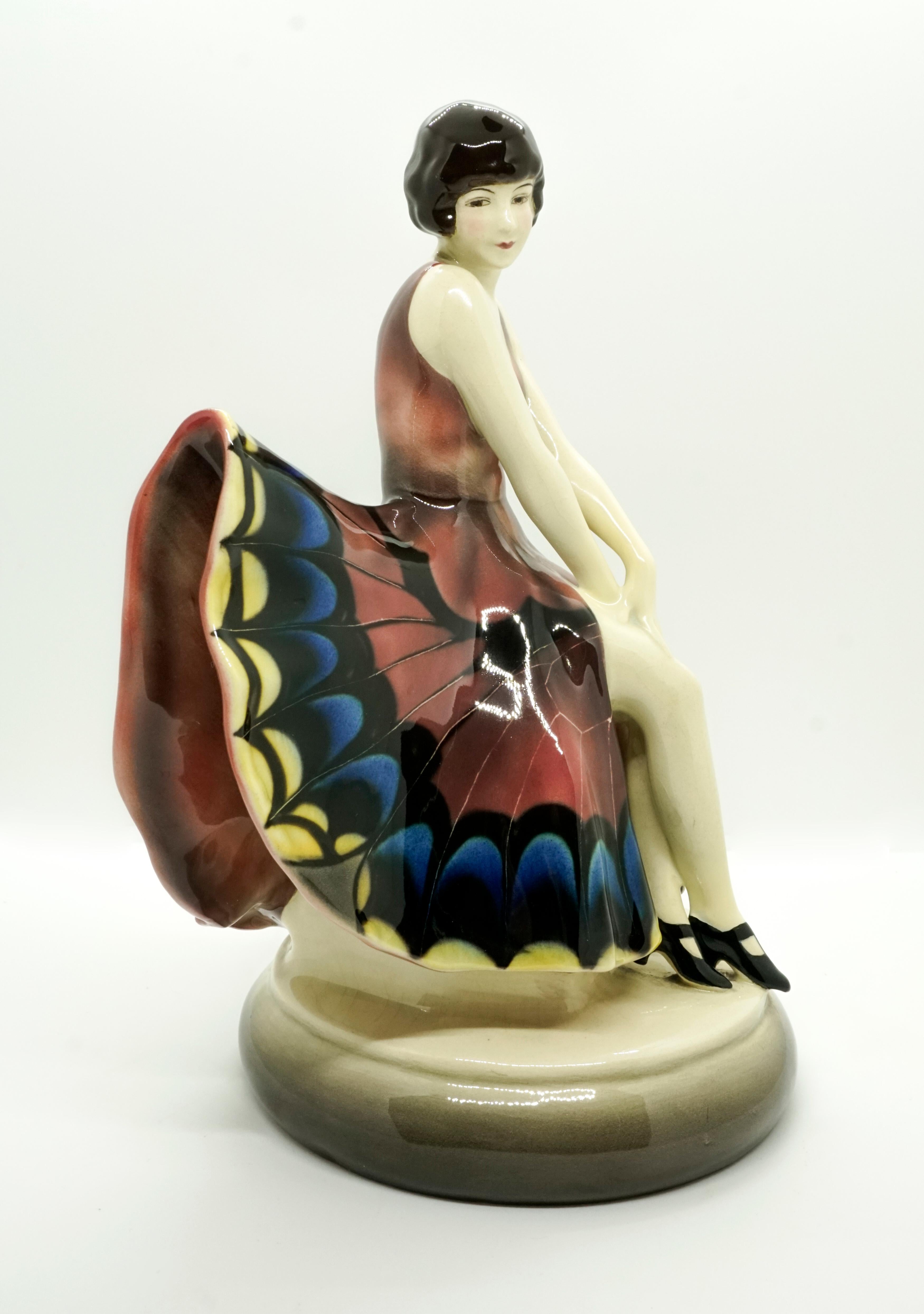 Rare Goldscheider ceramics figure of the 1920s.
The seated dancer wears a single-colored sleeveless top and a matching skirt that protrudes fan-like on both sides, on the front of which a colorful pattern is unfolded, which is modeled on butterfly