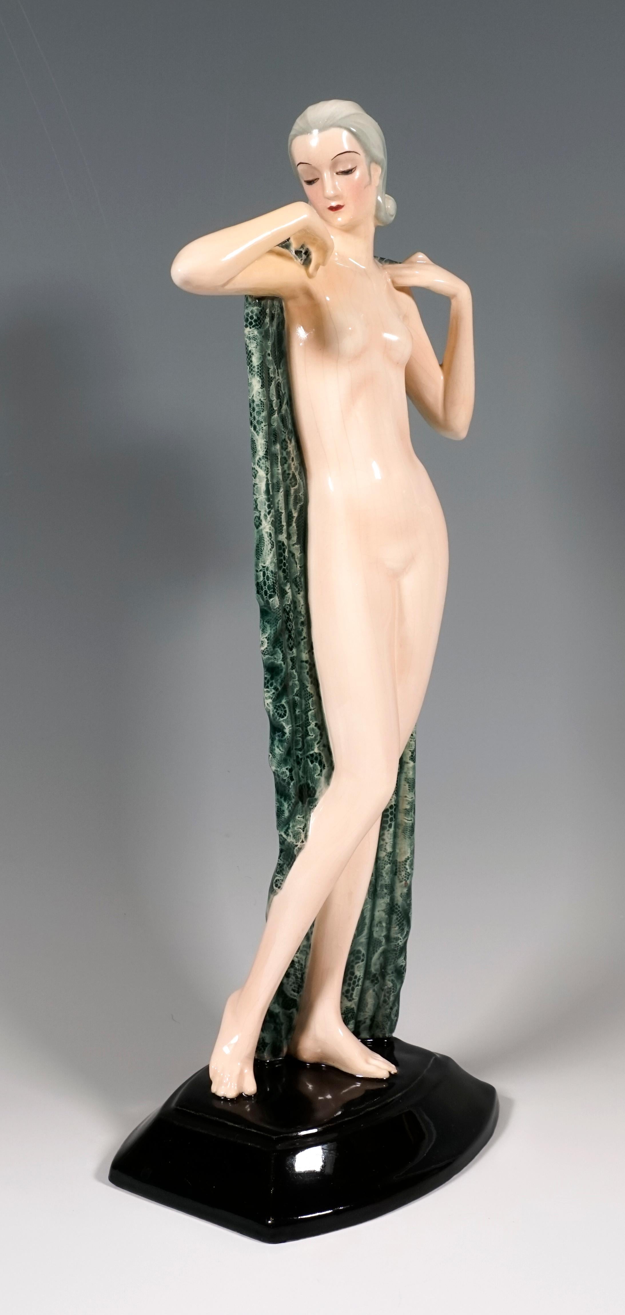 Sehr seltene Goldscheider Keramikfigur aus den 1930er Jahren:
Die stehende hübsche junge Frau mit zurückgekämmtem und im Nacken hochgestecktem Haar bedeckt ihre Blöße lediglich mit einem großen, grün-weißen Tuch, das sie hinter sich hält und das den