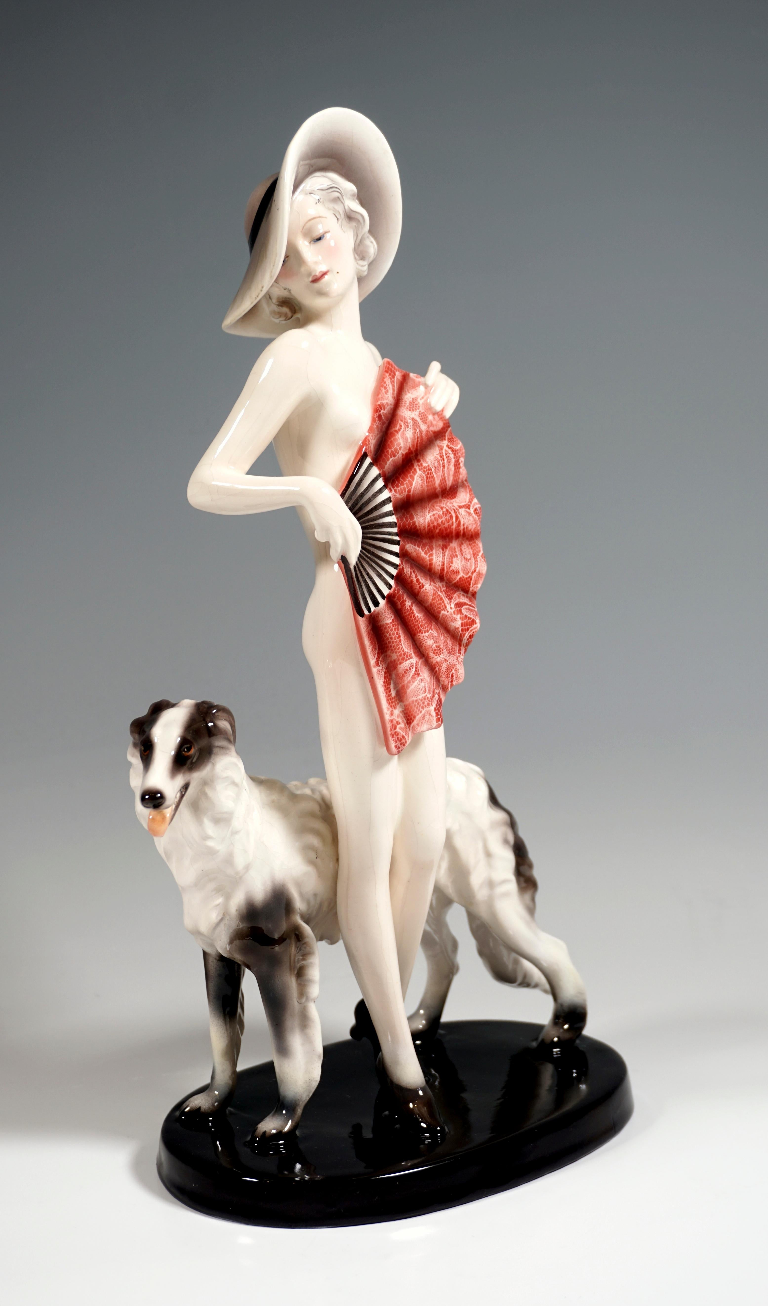 Very rare Goldscheider ceramic figurine of the 1930s:
Standing young pretty lady with a broad-brimmed hat on her curly, chin-length hair, wearing only heels and covering her nakedness with a large, red fan, which she holds in both hands in front of