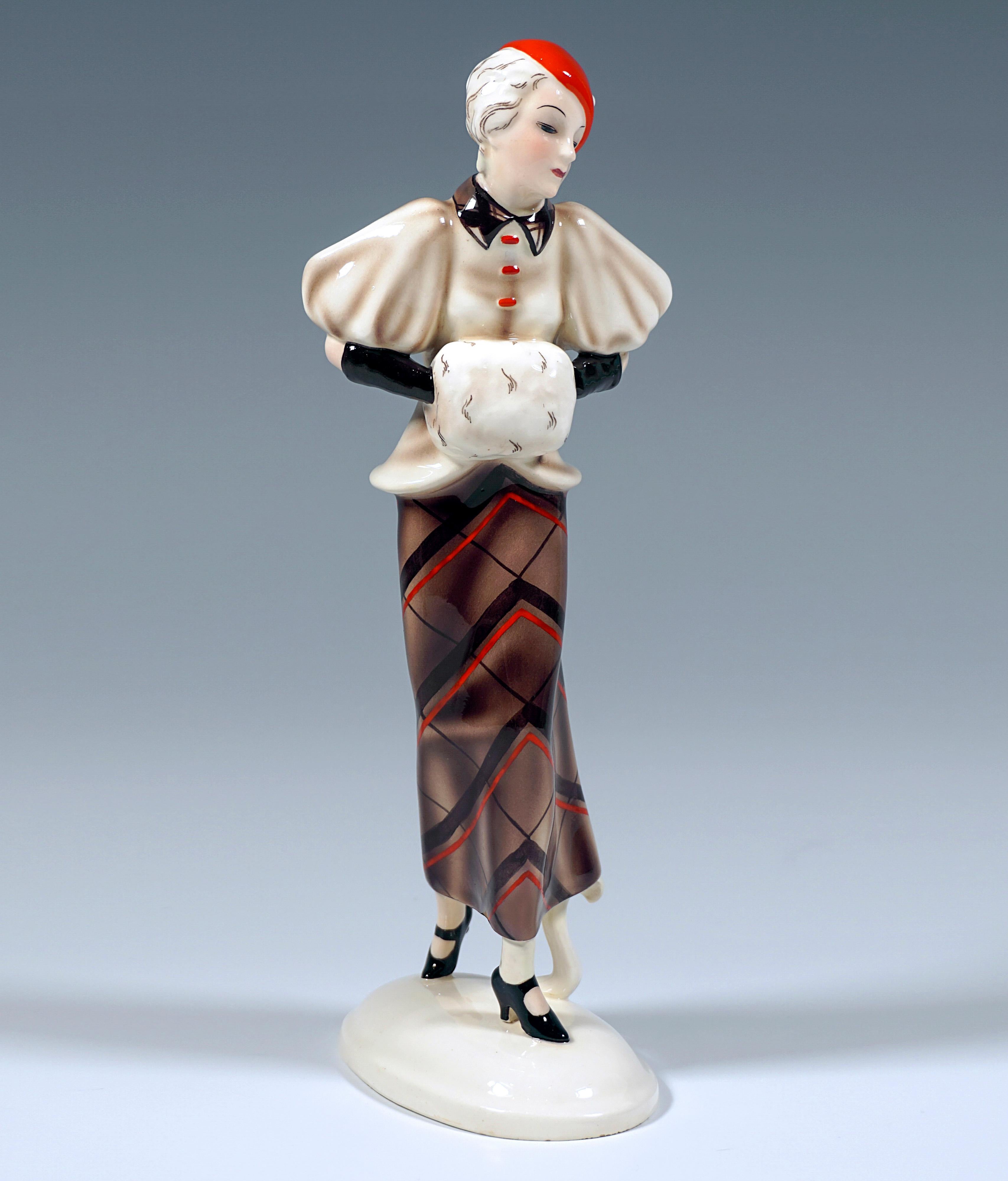 Sehr seltene Goldscheider Keramikfigur aus den 1930er Jahren:
Junge hübsche Frau mit kurzen Haaren und einem roten Hut, einem beigefarbenen Umhang mit weiten Puffärmeln und einem langen, engen Rock mit einem großen, braun-roten Karomuster, die ihre