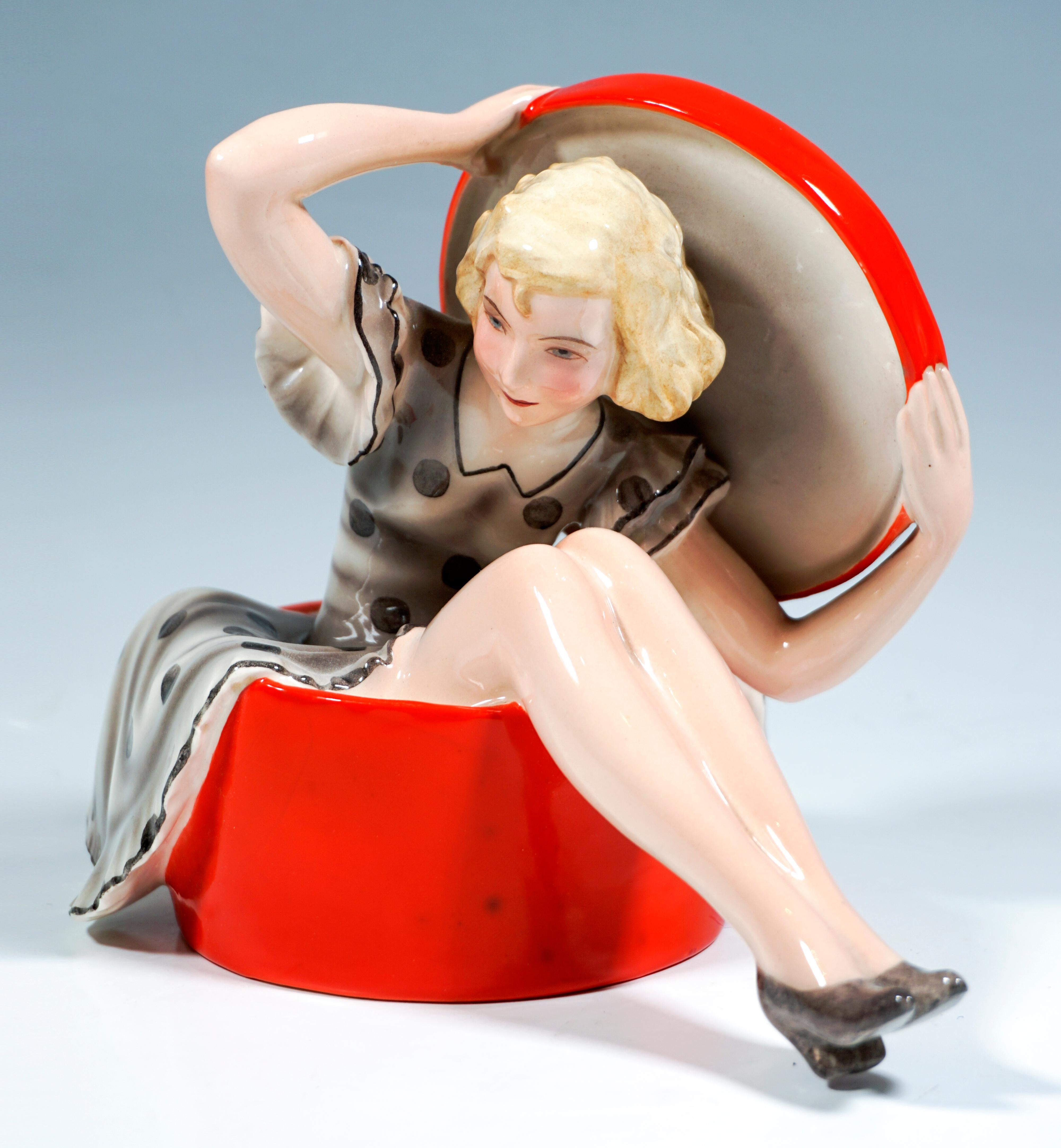 Rare Goldscheider Art Déco Ceramic Figurine.
Blond, curly-haired young lady in a light-grey, polka-dot summer dress sitting in a large, red hat box, leaning slightly forward, holding the lid in both hands behind her.
Without base, artist's