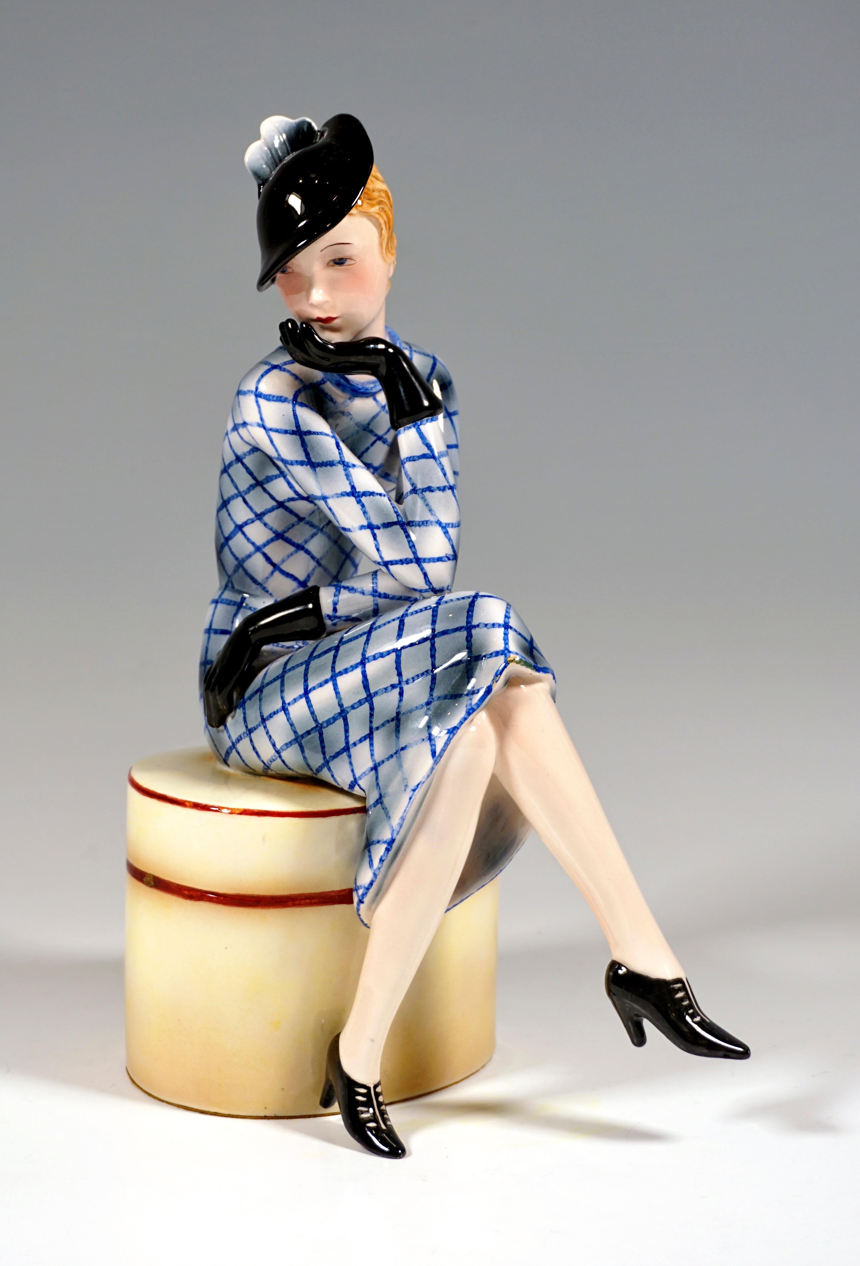 Very rare Goldscheider Art Deco Ceramic Figurine:
A young lady with red-blonde curly hair in an elegant, white-blue checked suit with a black hat, gloves and shoes sitting on a large, natural white hat box with dark red edges, crossed her legs,