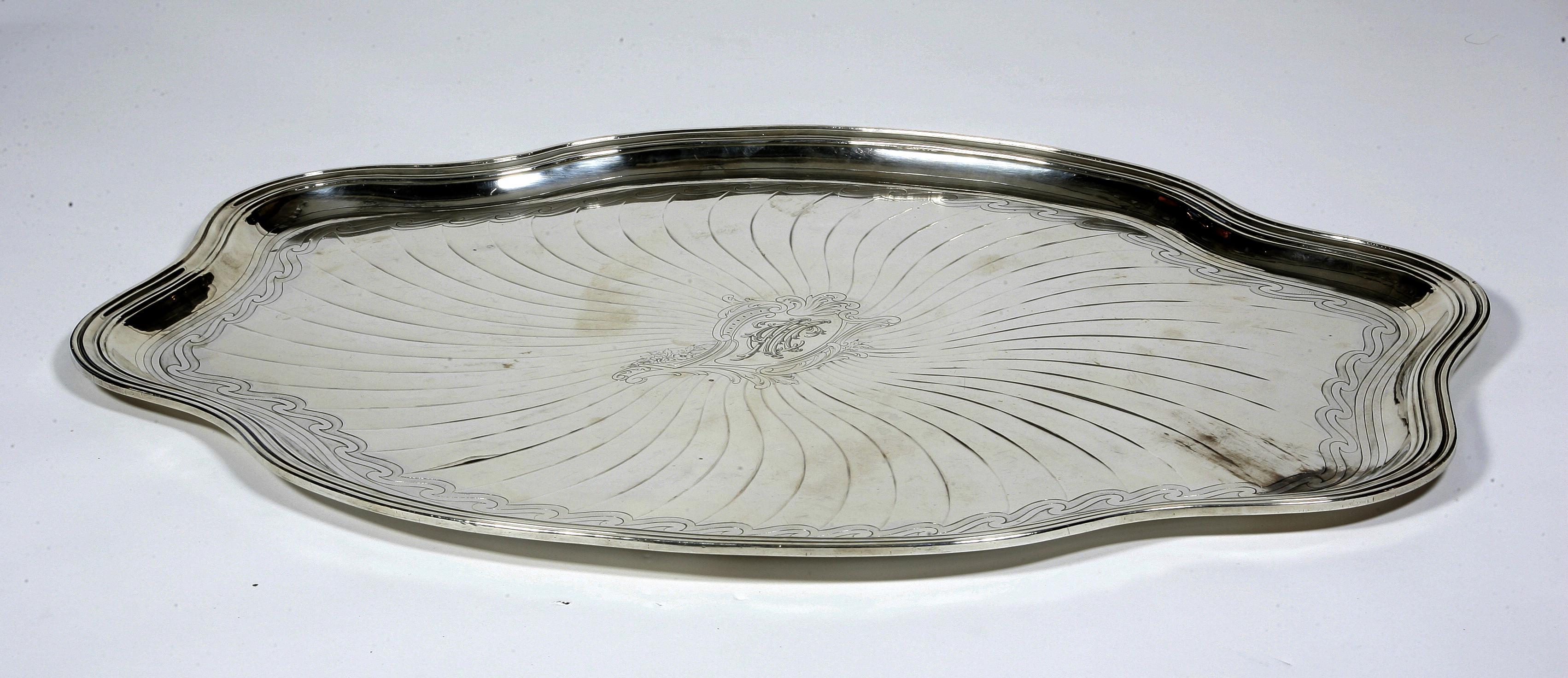 Large oval scalloped platter in solid silver with a belt of strong threads radiating decoration, in the center a stylized cartridge with an interlaced 