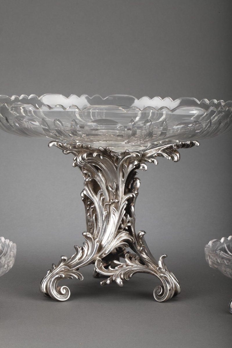 Juego de mesa formado por tres copas de plata maciza y cristal tallado. La base trípode de estilo balancín, con hojas de acanto y decoración arabesca, sostiene una copa de cristal tallado. A cada lado hay dos tallas inferiores con el mismo
