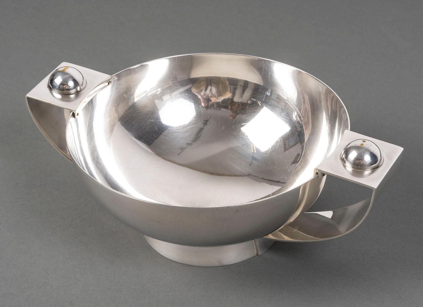 Plain round cup mounted on a 2 cm stick and flanked by two detached side handles

resting on the collar and fixed on the stick.

Dimensions: Inner diameter 21 cm - height 10 cm

Material: Silver metal

Goldsmith hallmark: CHRISTOFLE C C 2