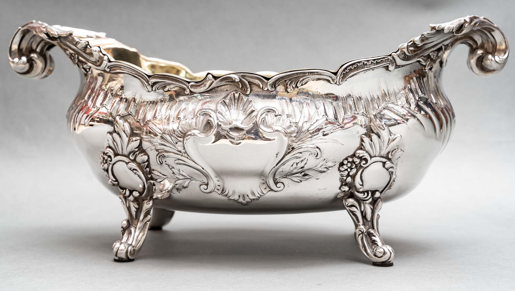 Oblong silver planter, resting on four claw feet in foliate crosier. The body is decorated with repoussé with a frieze of grooves. On the long sides is a rocaille cartouche surmounted by a shell. The integral handles are rolled up. The removable