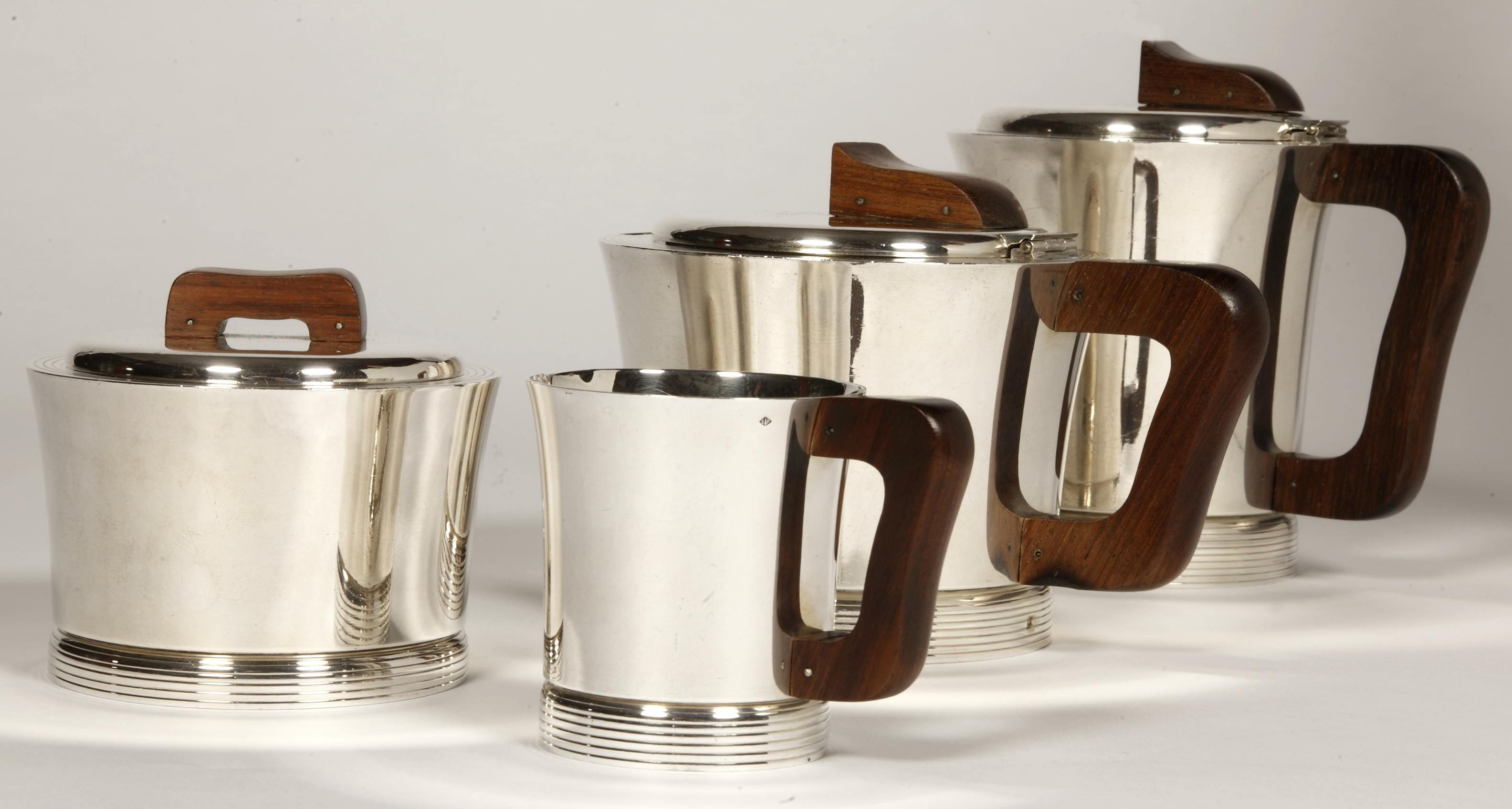 Service à thé / café composé d'une théière, d'une cafetière, d'un sucrier et d'un pot à lait, modèle DEAUVILLE, de forme ronde, le corps uni est fileté à la base et au col. les anses sont en bois (macassar) Dimensions hauteur : Théière 12,5 cm -