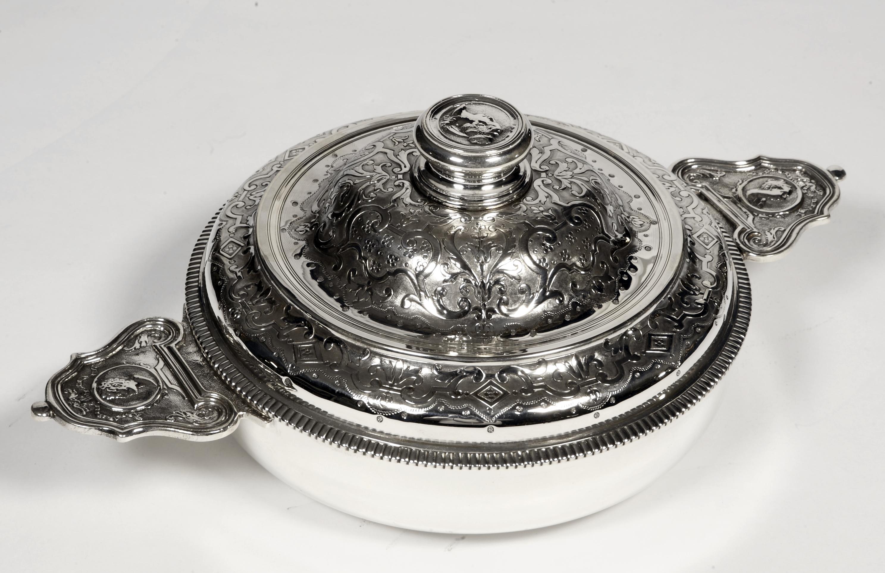 Silver vegetable dish in round shape. The plain body is flanked by two side handles with ears presenting a medallion on a chiseled amati background with a man's head on one side and a woman's head on the other. The lid with circumference of
