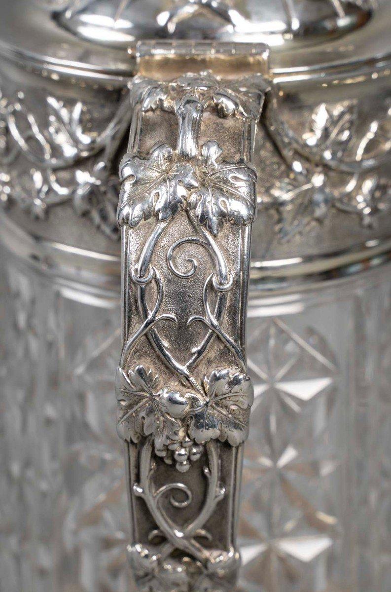 Important PITCHER in diamond-cut crystal, inserted in a large silver setting connected by a handle at the neck and closed by a hinged lid topped with a fret. Rich carved decoration of vines, vine leaves and bunches of grapes on matted backgrounds.