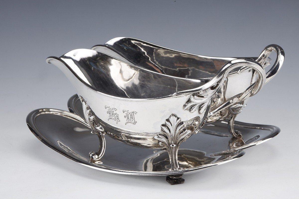 Salsera doble de plata maciza decorada lisa, montada sobre cuatro patas foliadas, con monograma, colocada sobre una bandeja adherente.
Dimensiones: anchura 26 cm - profundidad 20 cm - altura 12 cm
Material: plata de 1ª ley 950/°°°.
Peso: 1288