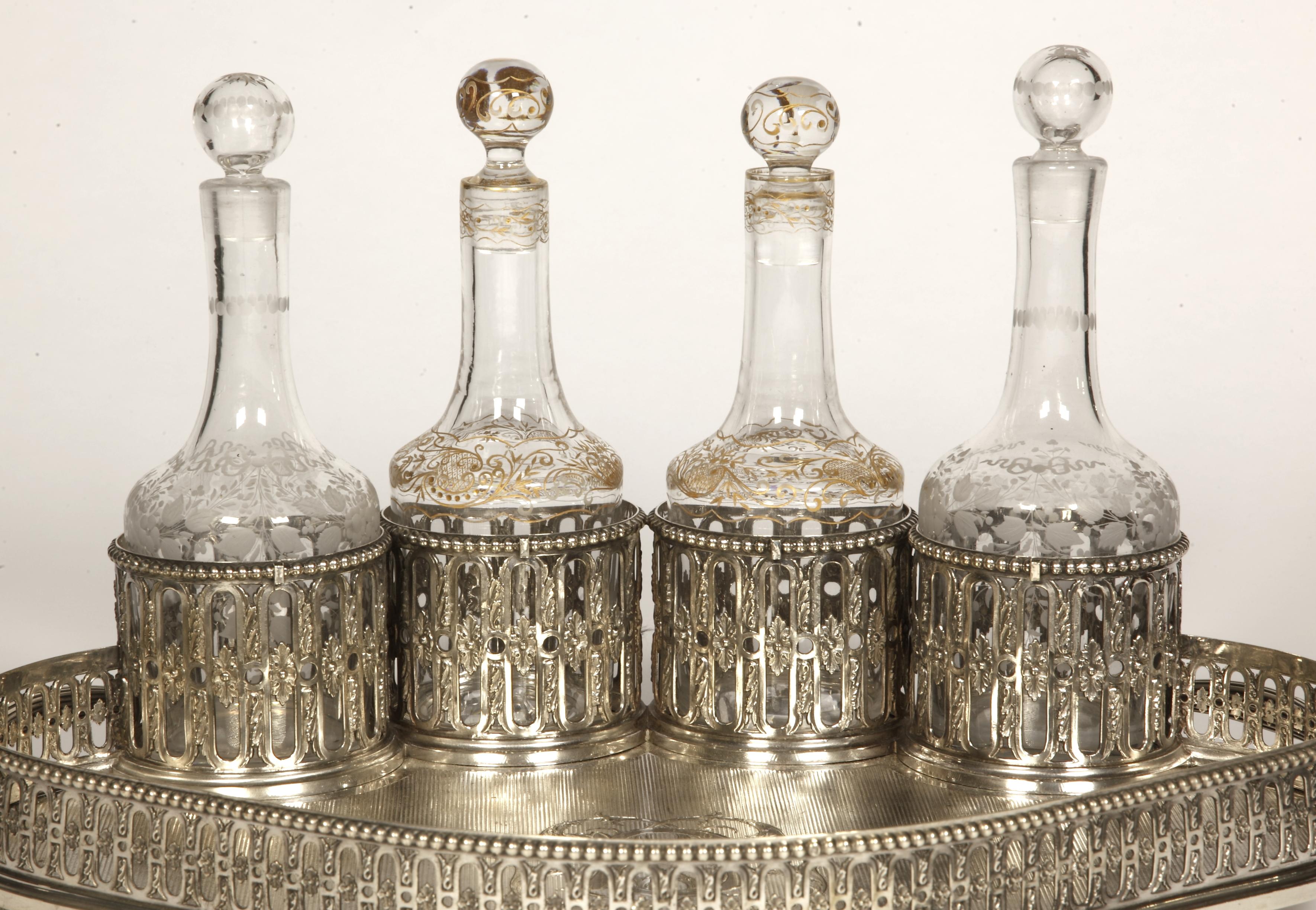 Cabaret à liqueurs en argent massif composé d'un plateau guilloché animé, monté sur quatre pieds boules, entouré d'une large galerie ajourée, présentant quatre gobelets contenant quatre bouteilles en cristal. bouteilles postérieures, au centre du