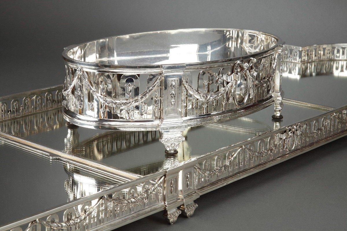 SURTOUT DE TABLE in solid silver with mirror bottom on wooden floor; rectangular in shape, with half-moon ends, the openwork belt pierced with arches is decorated with laurel garlands held in the center by an armorial medallion and punctuated by