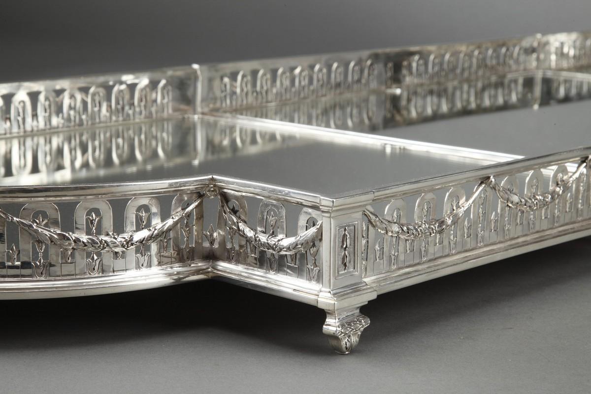 Solid silver surtout de table  with a mirrored back on a wooden parquet; rectangular in shape with half-moon-shaped ends,

the openwork apron, pierced with arches, is decorated with laurel garlands held in place in the center by a medallion with a