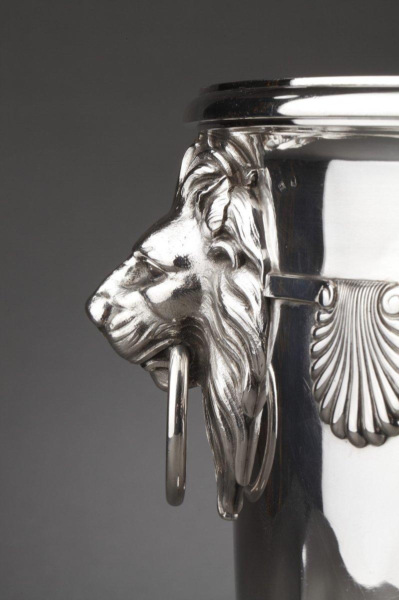 Solid silver cooler mounted on an ogee pedestal. The plain body is decorated with applique seashells, flanked on either side by a zoomorphic grip represented by a lion's head holding a ring. The collar is surrounded by a simple bead. Silverware