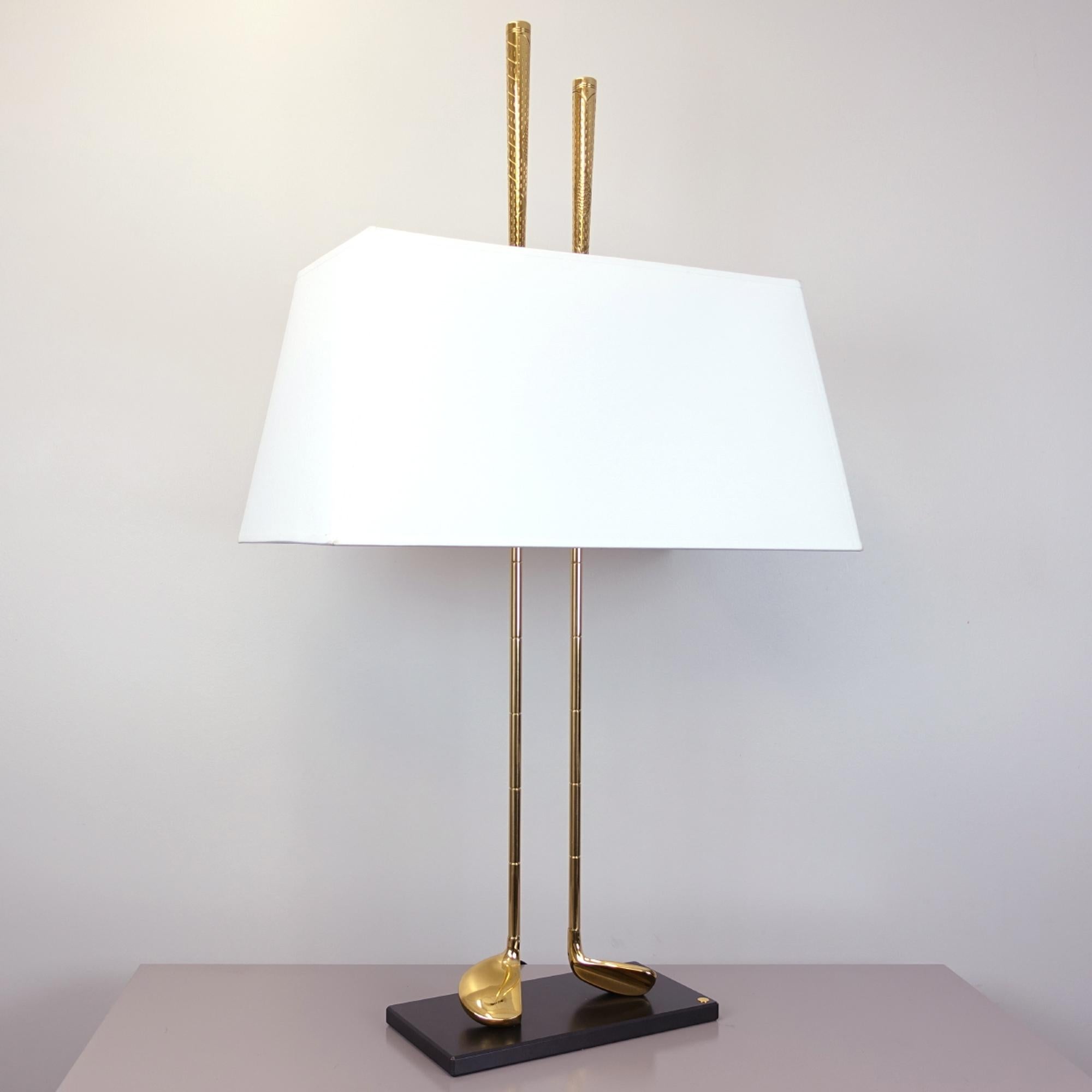Table lamp Golf Club with 2 clubs in brass in
polished brass finish. With white shade 
included. 2 bulbs, lamp holder type E14,
max. Limited Edition. Edition of 100 pieces.
Made in France.
With customizable plaque to write a name
or a company,