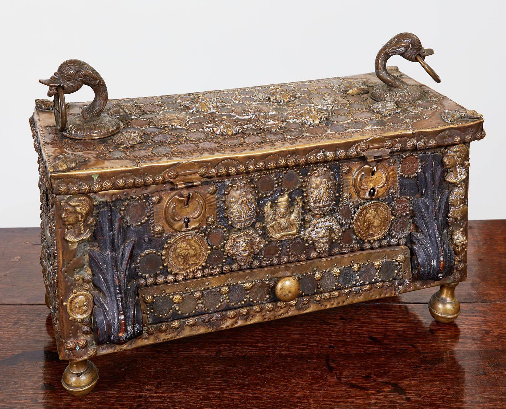 A Venetian gondolier's coin-encrusted money box consisting of a leather clad wooden case profusely decorated with brass studding, applique period coins, busts and masks, carved wooden corbels and two fabulous goose-head ring mounts to top surface.