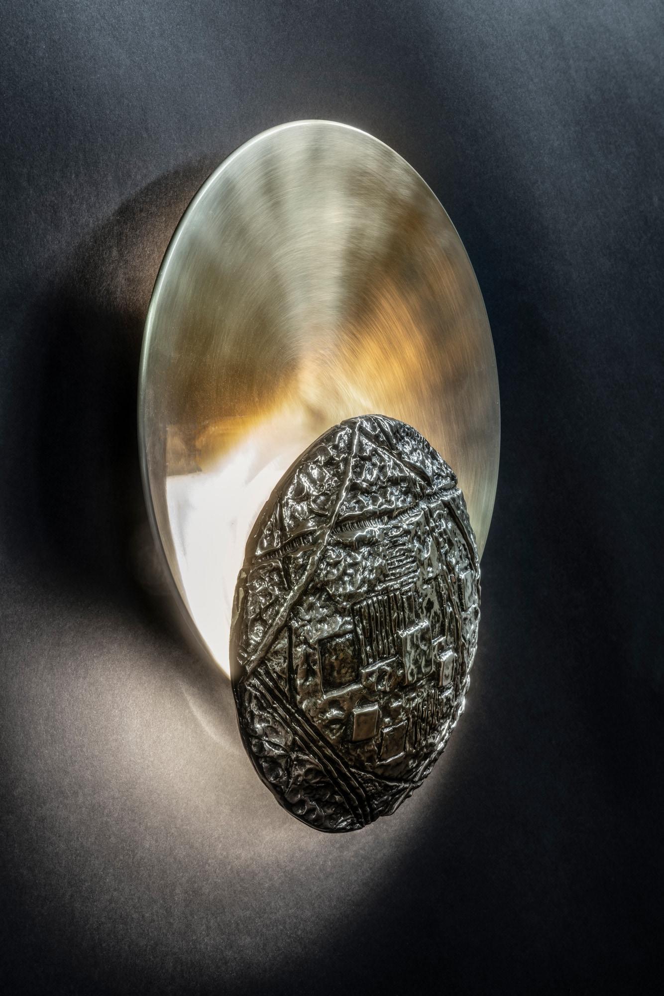 Wall lamp consisting of a larger circular volume in satin brass and another volume in decorated brass casting.