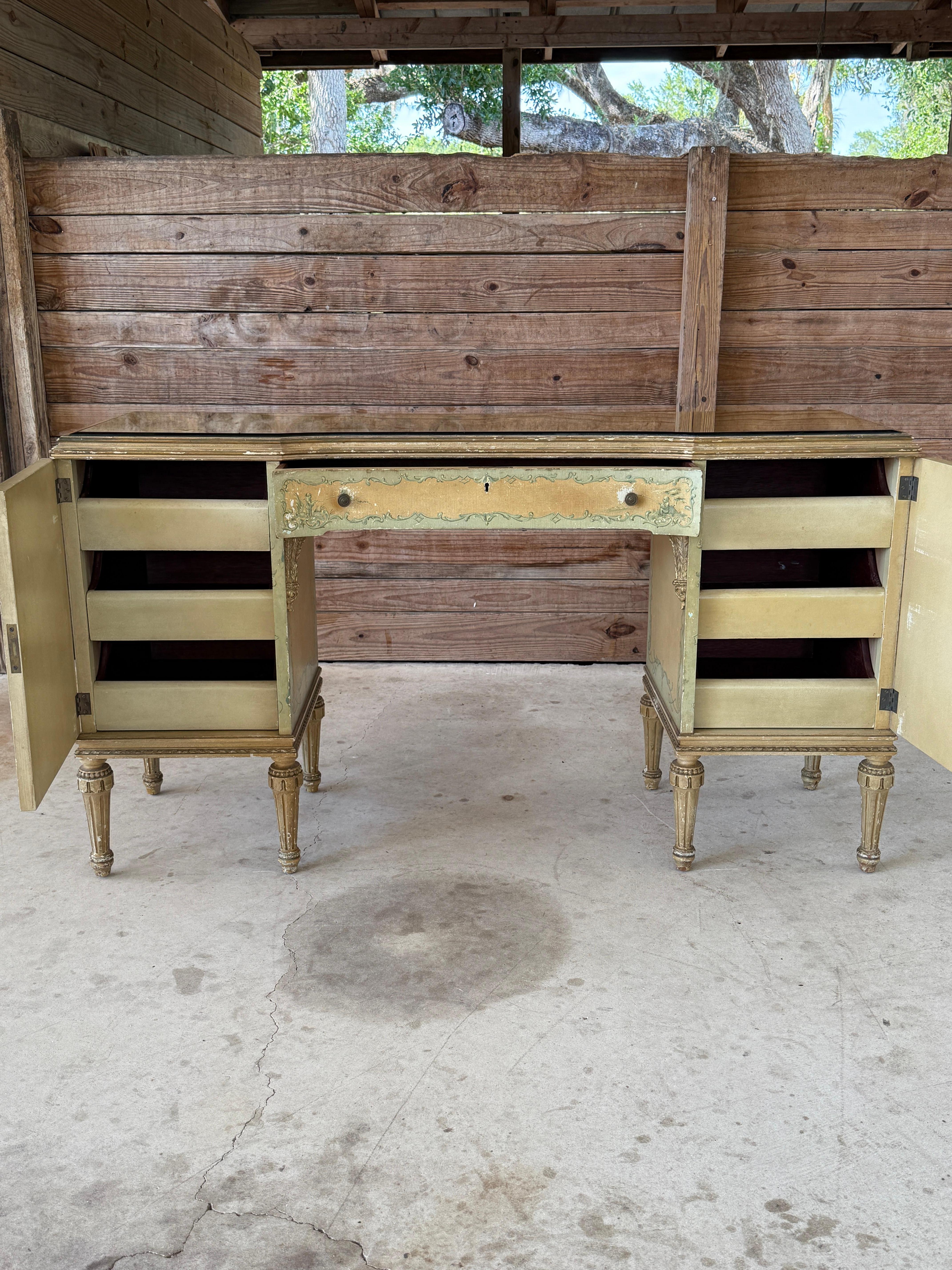 A charming Mid-20th Century hand-painted desk or vanity crafted by Hampton Shops of New York. This elegant piece reflects a Venetian Revival style, showcasing chinoiserie-inspired scenes framed by scrolling foliate motifs, all rendered in soft green