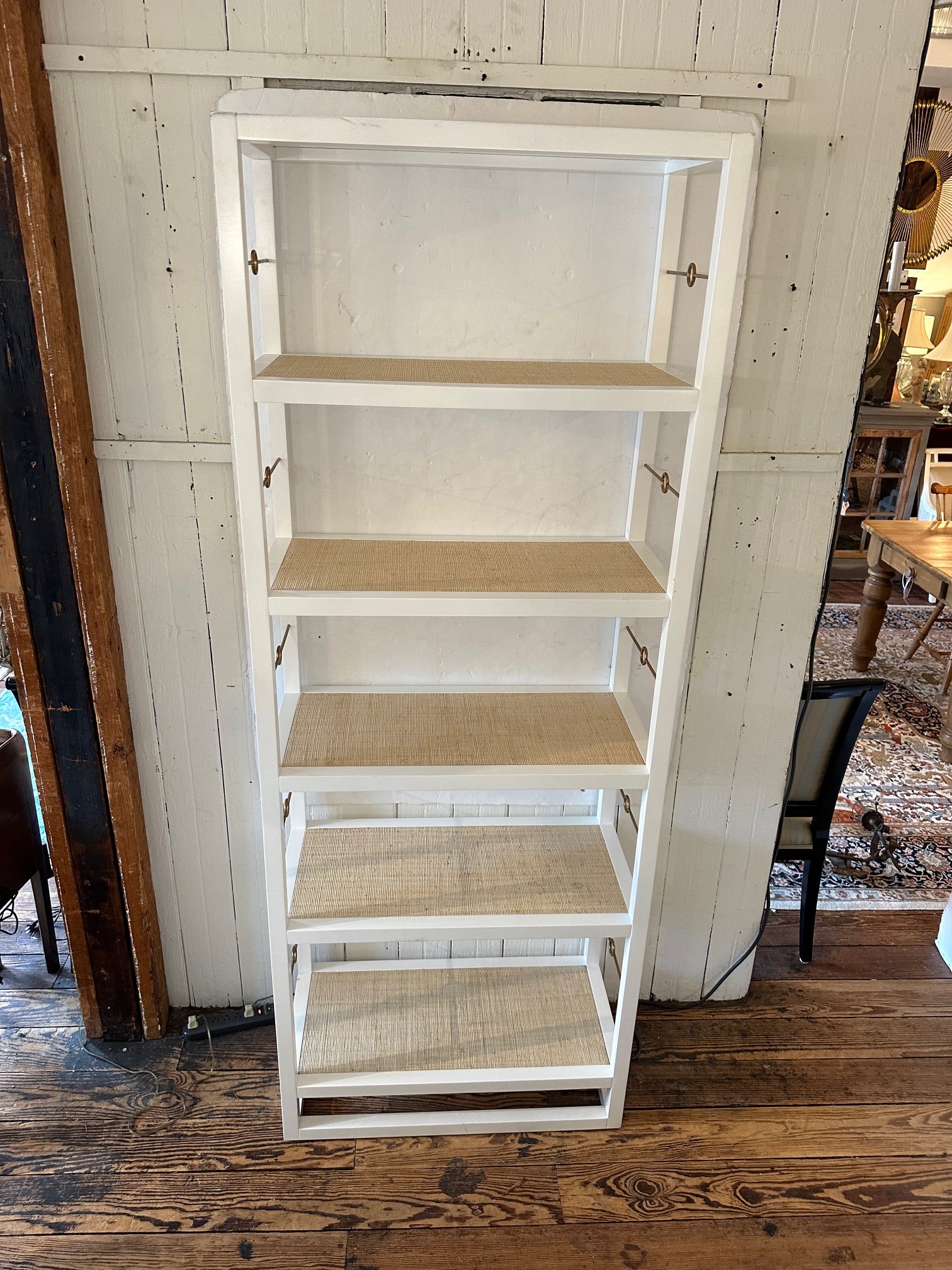Estupenda y funcional estantería de madera pintada de blanco y 5 baldas forradas de tela de hierba con barras laterales decorativas de latón.

Los estantes tienen 15