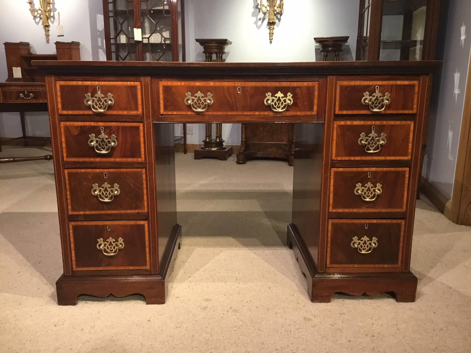 A good mahogany inlaid Edwardian Period pedestal desk. Having a mahogany rectangular top banded in satinwood and with an inset red leather writing surface with gilt tooled detail. With an arrangement of nine oak lined drawers with flamed mahogany