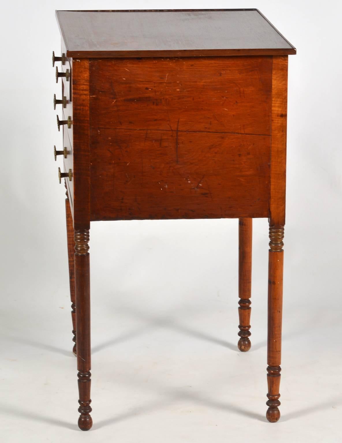 Of elegant proportions and great craftsmanship this Pennsylvania tiger maple and walnut work table features a tray edged top above three graduated drawers supported by slender circular turned legs.