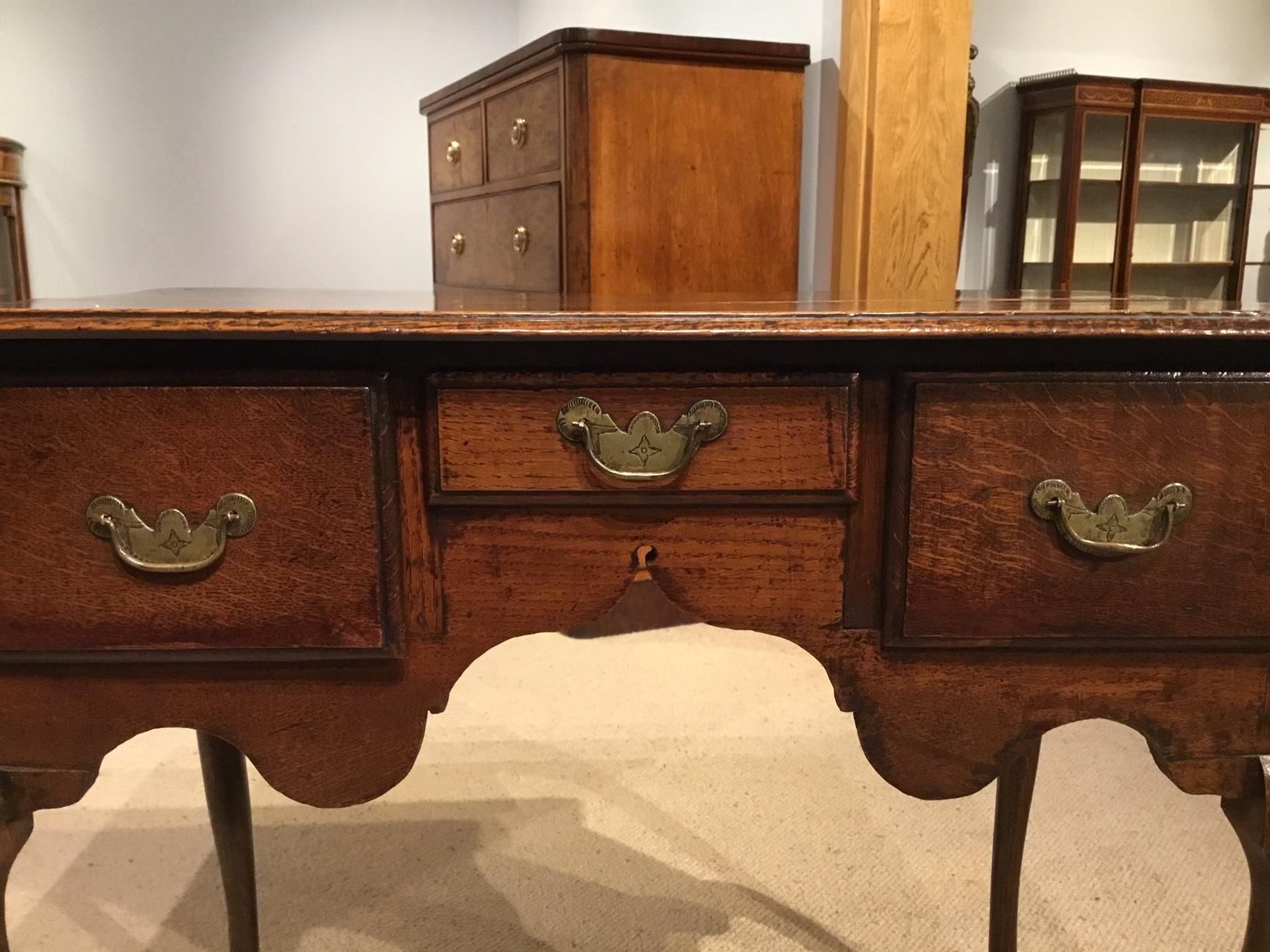 A good oak George III Period lowboy. Having a rectangular oak two plank top of superb colour and patination above three rectangular oak drawers retaining the original brass handles and back plates. With a wavy frieze and supported on elegant