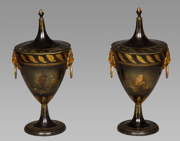 A delightful pair of Regency period tole-work covered chestnut urns in good original condition with very minor in-painting. Each is painted to one side with a naval scene, to the other with a house in a rural landscape, and both with twin lion's
