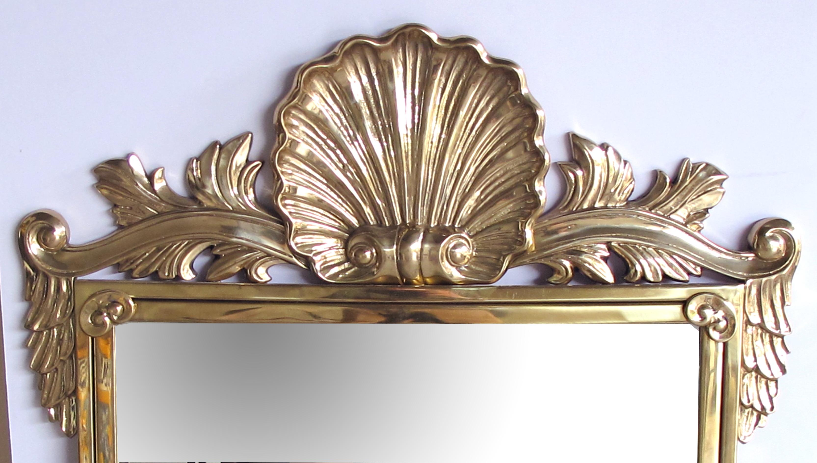 A good quality Italian Hollywood regency solid brass mirror with over-scaled shell crest by Decorative Crafts, Inc. est. 1928; in the neoclassical taste, the boldly-scaled solid brass crest centring a robust shell motif flanked by lively scrolls and
