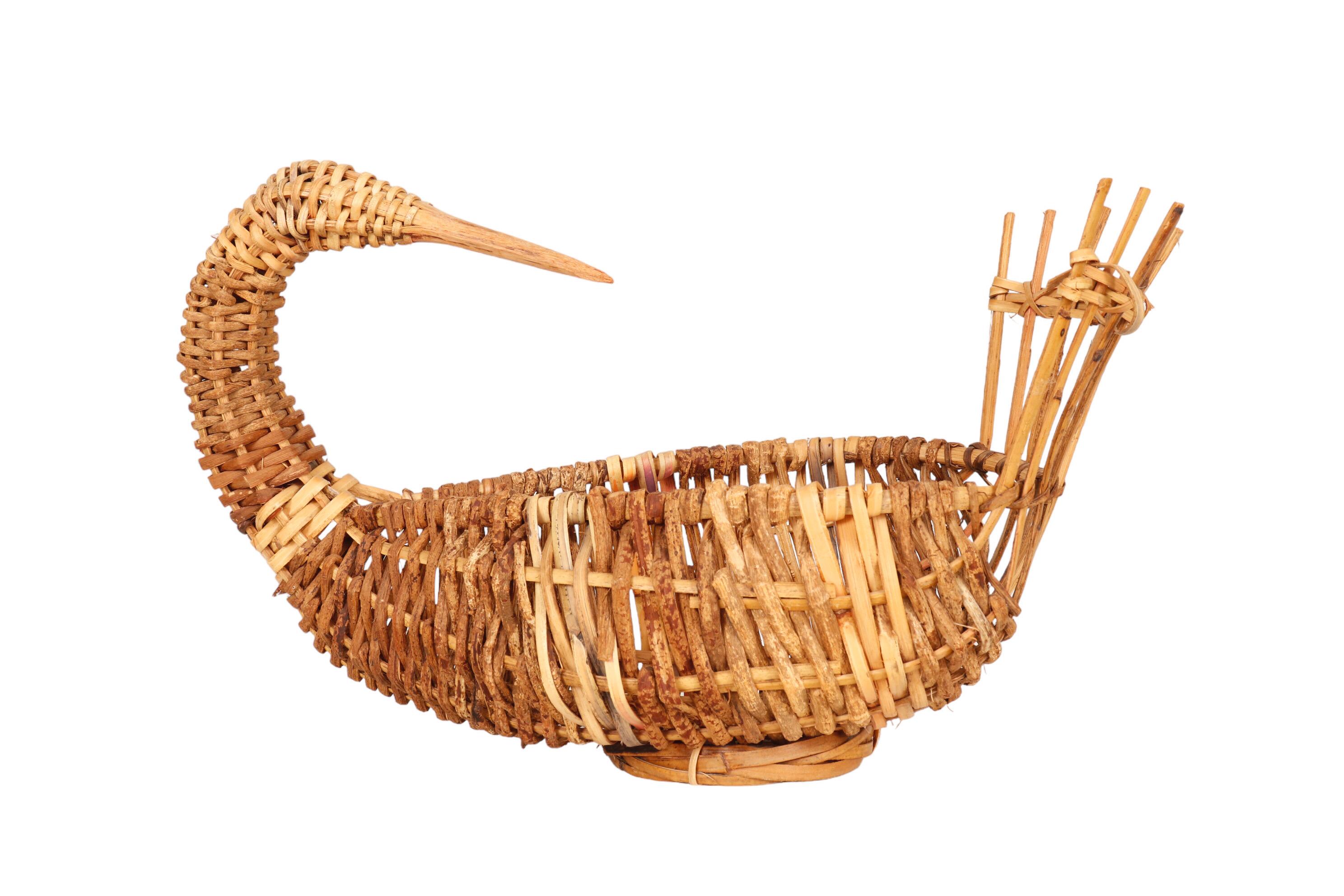 A woven rattan basket shaped like a goose. A long neck curves around and turns back to face long raised feathers. A beak is formed from where the rattan joins into a single piece, and lighter bands decorated the neck and body. Inside are strands of