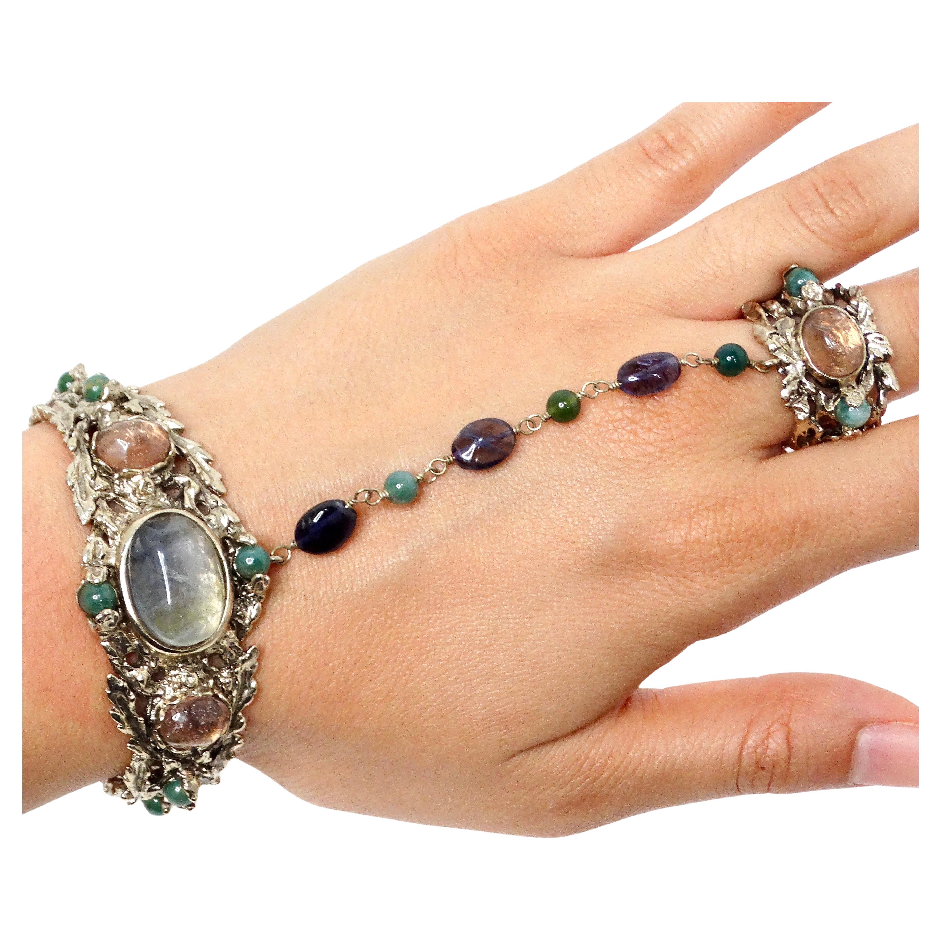 Das Goosens Paris Ornate Gemstone Hand Chain Cuff Bracelet mit Ring ist ein atemberaubendes Statement, das exquisite Handwerkskunst und künstlerisches Design verkörpert. Die Manschette aus edlem, silberfarbenem Metall ist mit filigranen,