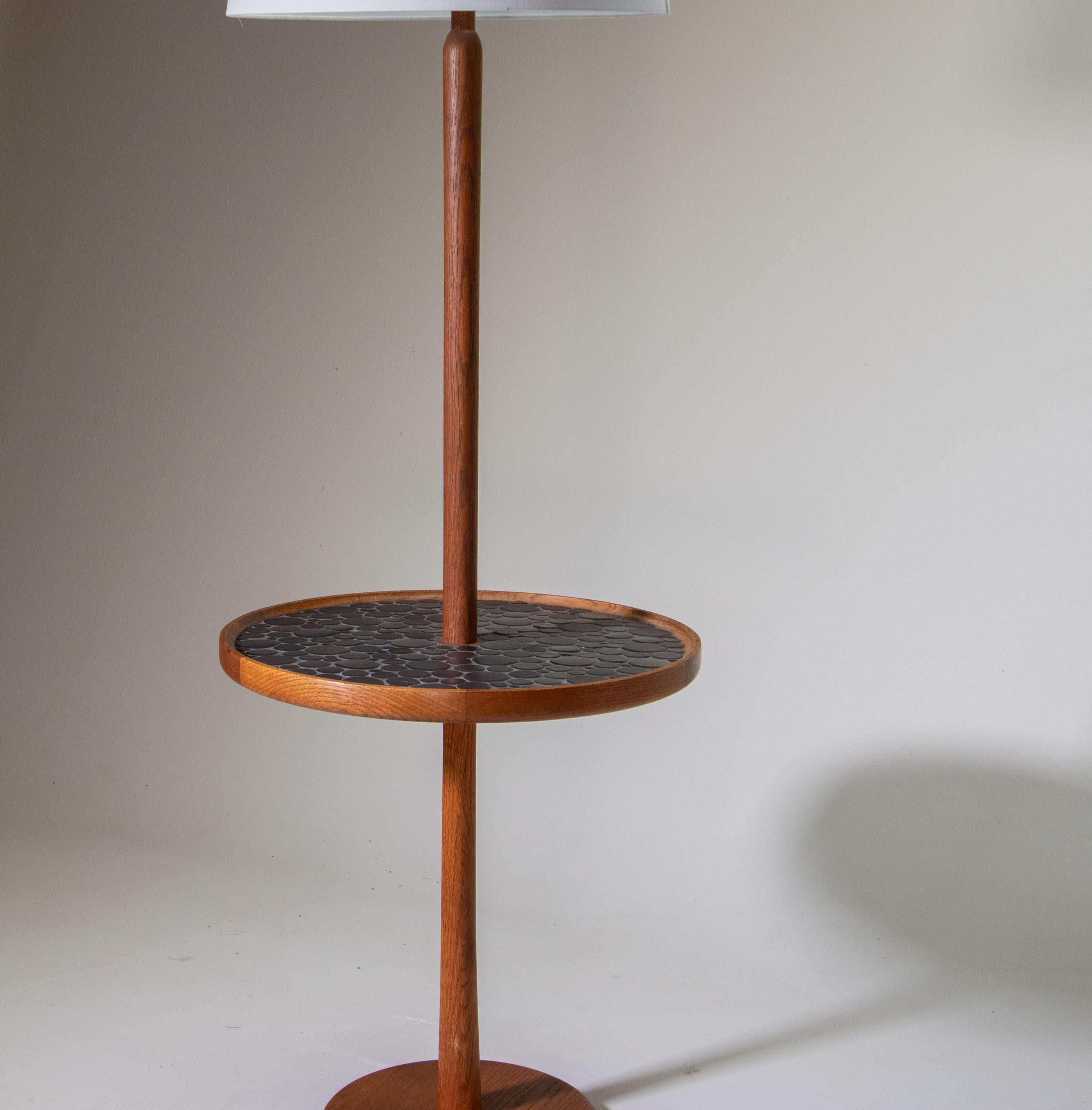 A 1960s W4 floor lamp designed by Jane and Gordon Martz for Marshall Studios featuring coin shaped tiles in a gray color way. The tile table features a solid teak raised lip around the table portion as well solid teak stem and base. A great lamp in
