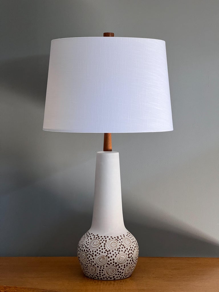 Beautiful ceramic table lamp designed by Jane and Gordon Martz for Marshall Studios, c. 1960s. This examples shows off a lovely flat white glaze with incised swirls and dots. Walnut neck and finial. New shade and socket. Signed “martz” 

Overall