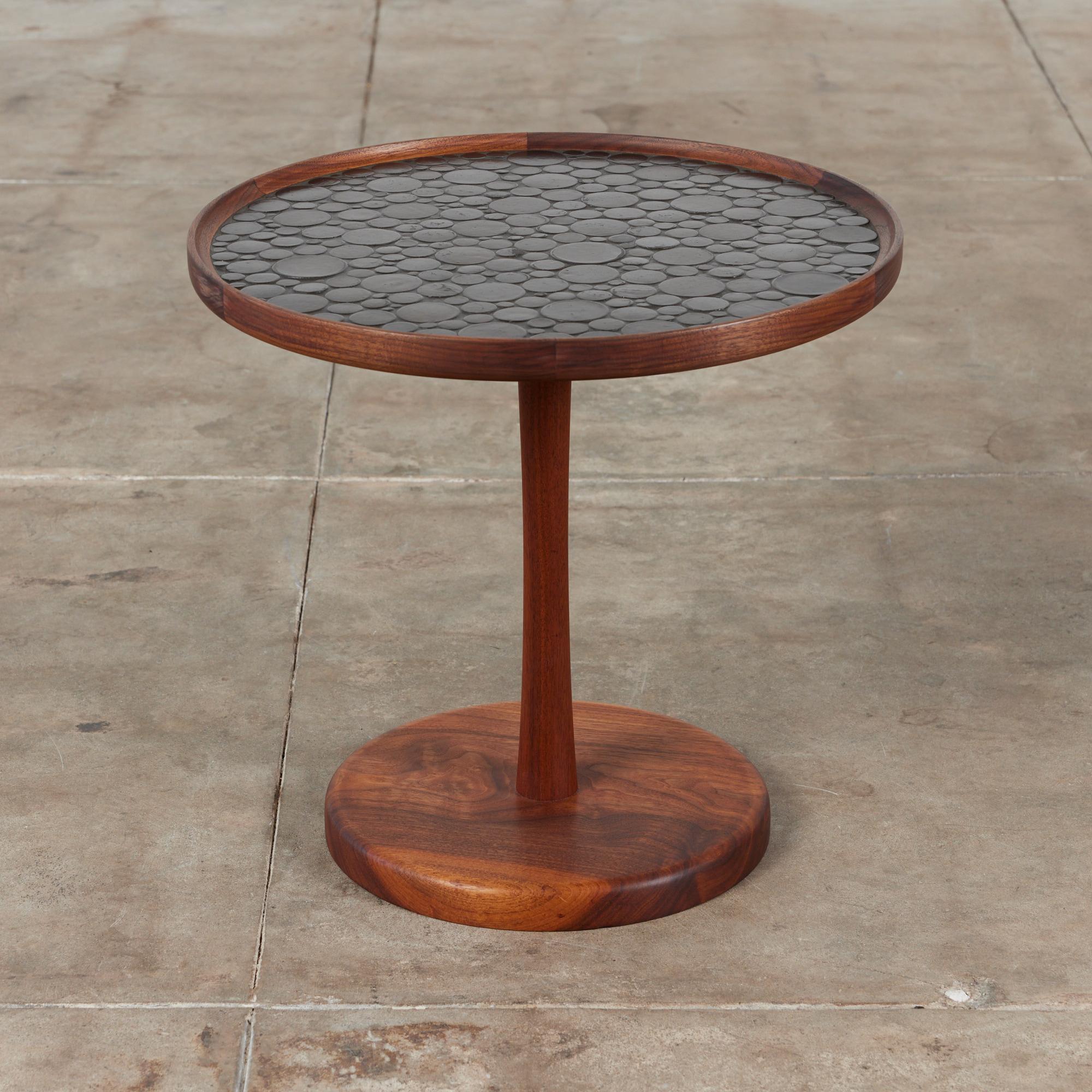 Round side table by Gordon & Jane Martz. The table top is inlaid with black ceramic coin tiles. The frame, base and pedestal of the table are all solid walnut.

Dimensions
20