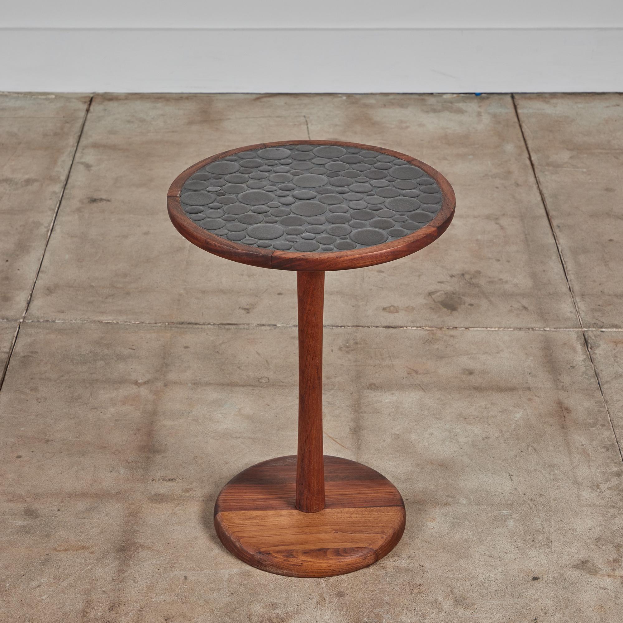 Round side table by Gordon & Jane Martz. The table top is inlaid with black ceramic coin tiles. The frame, base and pedestal of the table are all solid walnut.

Dimensions: 14