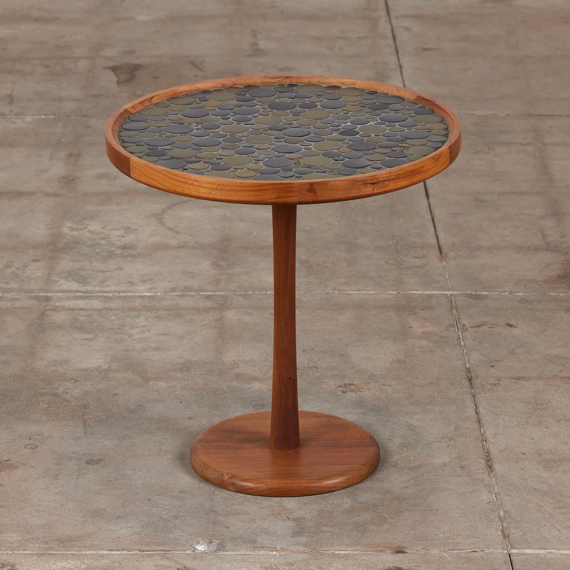 Round side table by Gordon & Jane Martz. The table top is inlaid with ceramic coin tiles in varying brown and black tones. The frame, base and pedestal of the table are all solid walnut.

Dimensions: 20.25