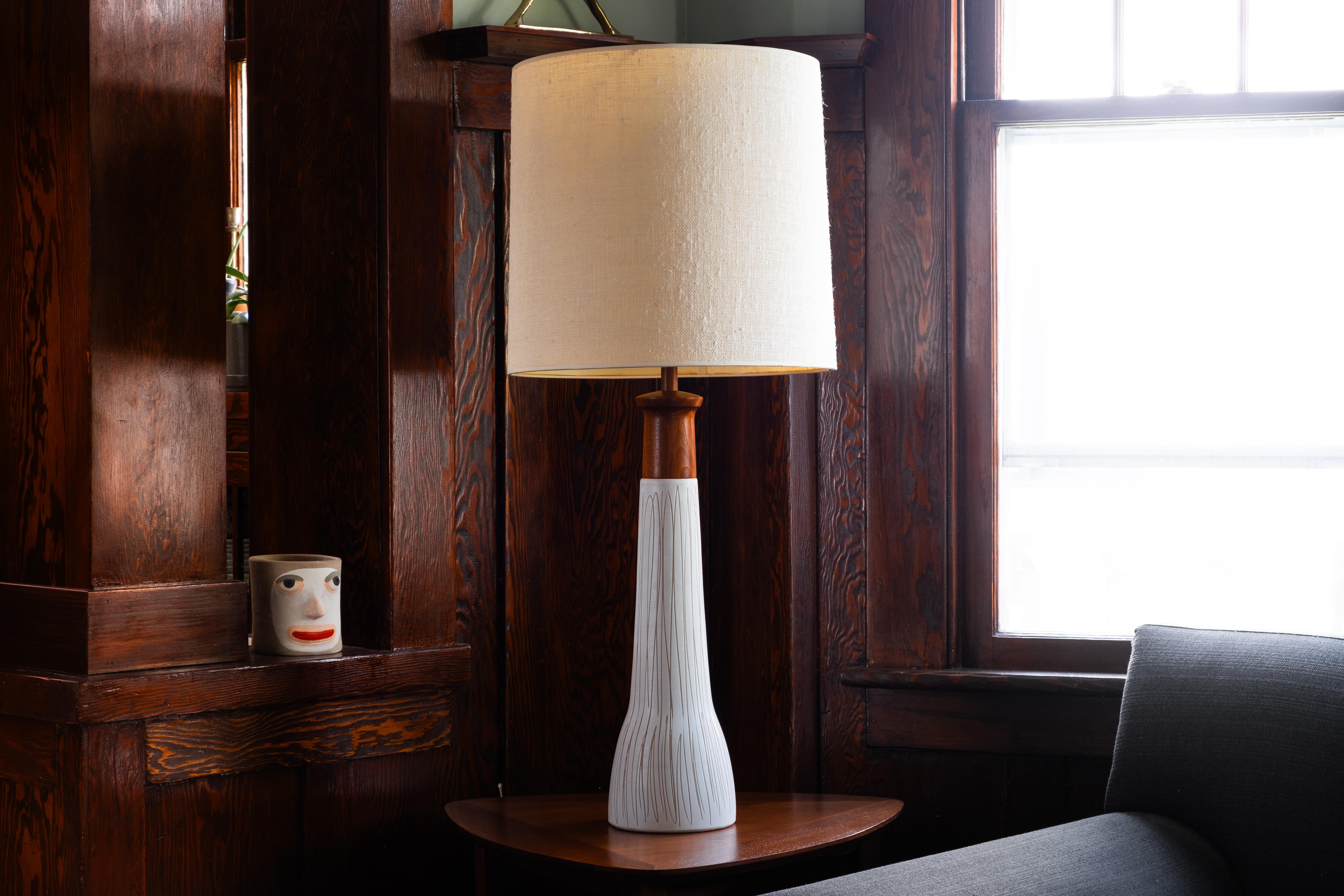 WHAT IS IT?
—
This pair of Martz model no. 165-28-1 lamps arrives with white glaze bodies that are decorated with a top-to-bottom incised line pattern. The lamps are topped off with large, turned sculptural walnut necks. The glaze of the lamps is