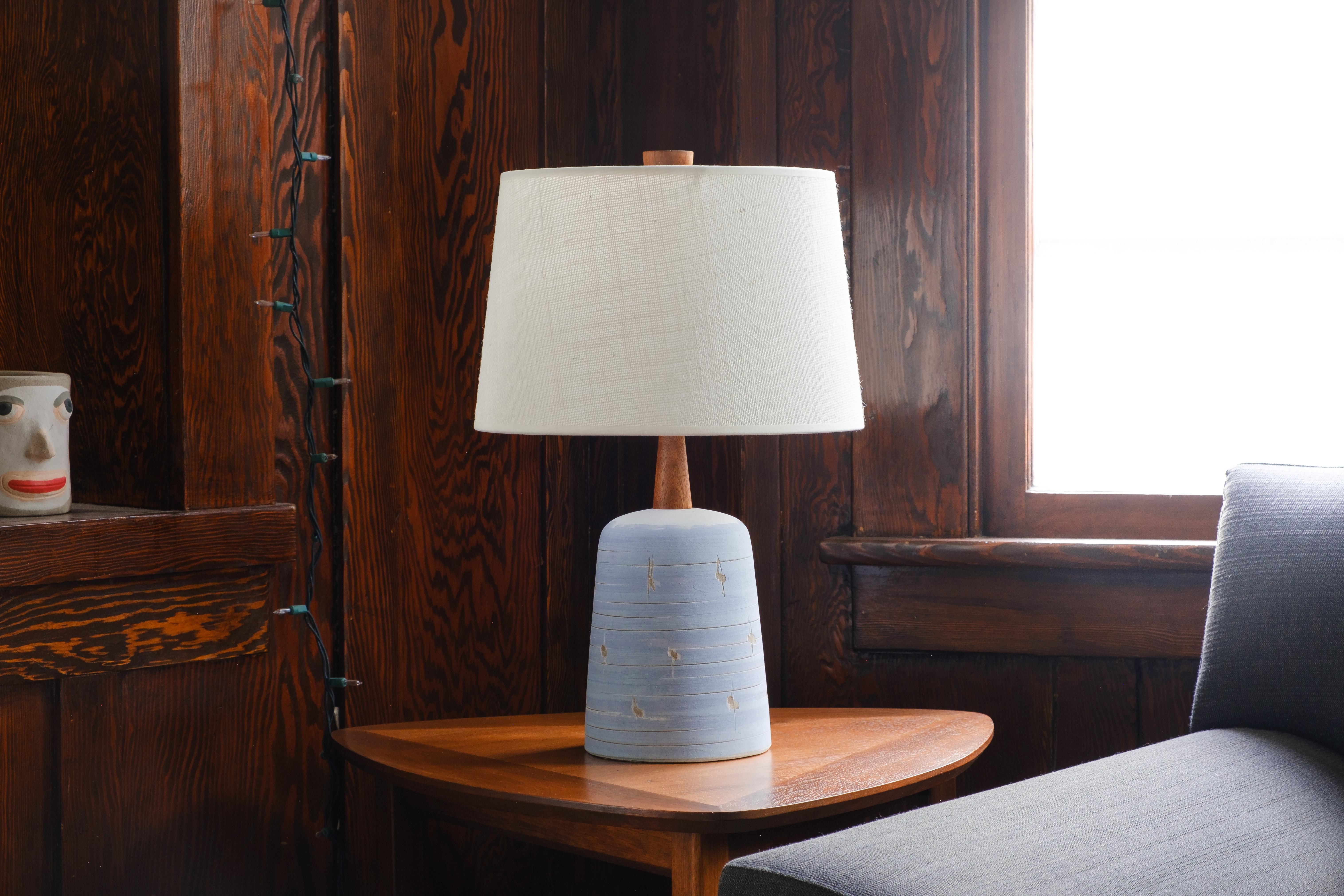 WHAT IS IT?
—
These signed Martz #56 lamps come in a flat, white slip with a horizontal swirl stripes of a blue slip. The body is further decorated with a repeating pattern of horizontal incised swirls and 