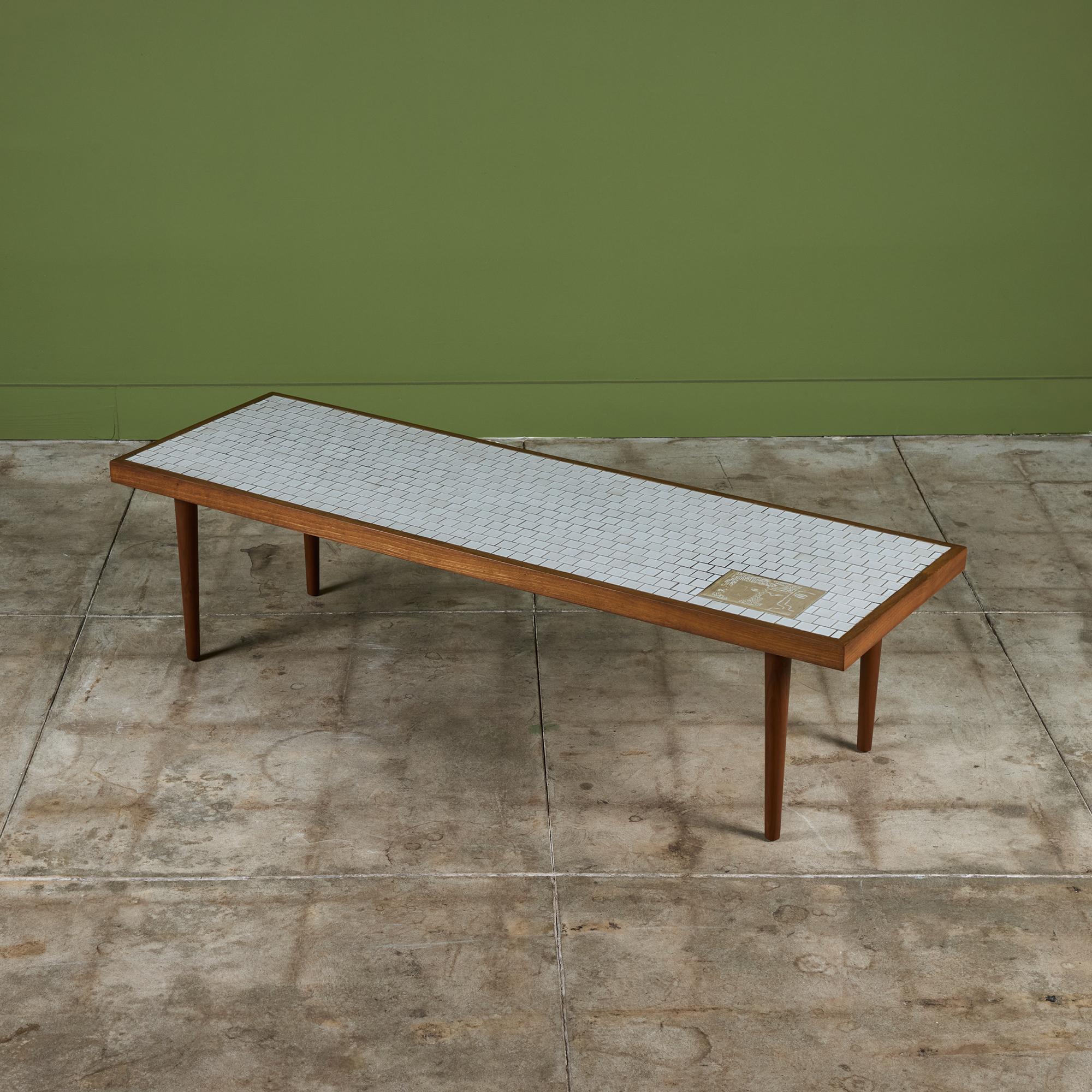 Rectangular coffee table by Gordon & Jane Martz for Marshall Studios. The table top is inlaid with white square ceramic tiles and a single large rectangular tile with abstract faces. The frame of the table and four legs are solid