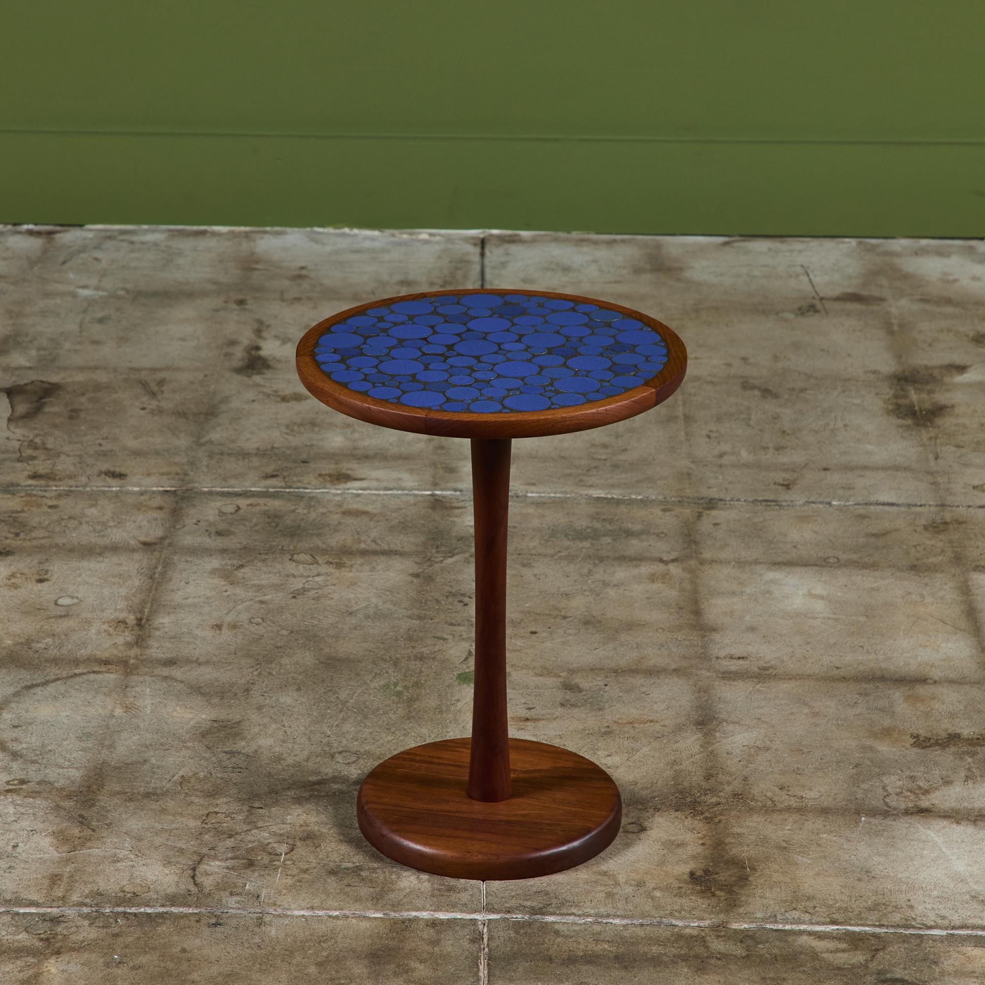 Round side table by Gordon & Jane Martz. The table top is inlaid with ceramic coin tiles in a royal blue glaze. The frame, base and pedestal of the table are all solid walnut.

Dimensions
14