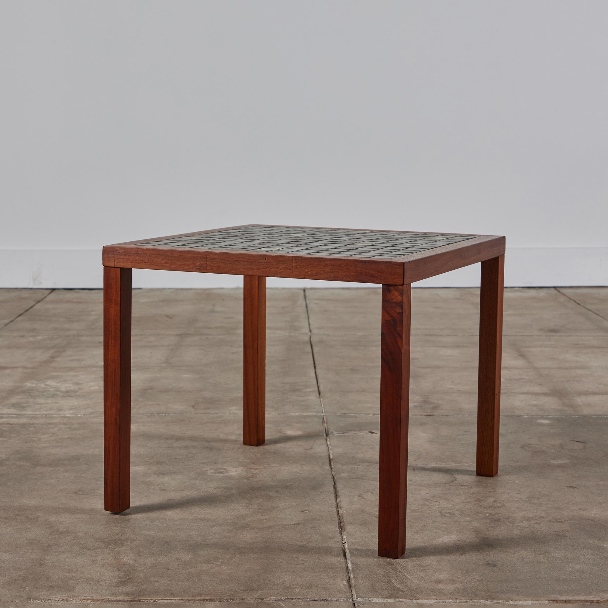 Square side table by Gordon & Jane Martz. The table top is inlaid with square ceramic tiles in dark gray with six cream, dark brown and green tiles placed randomly throughout the table. The frame of the table and four legs are solid