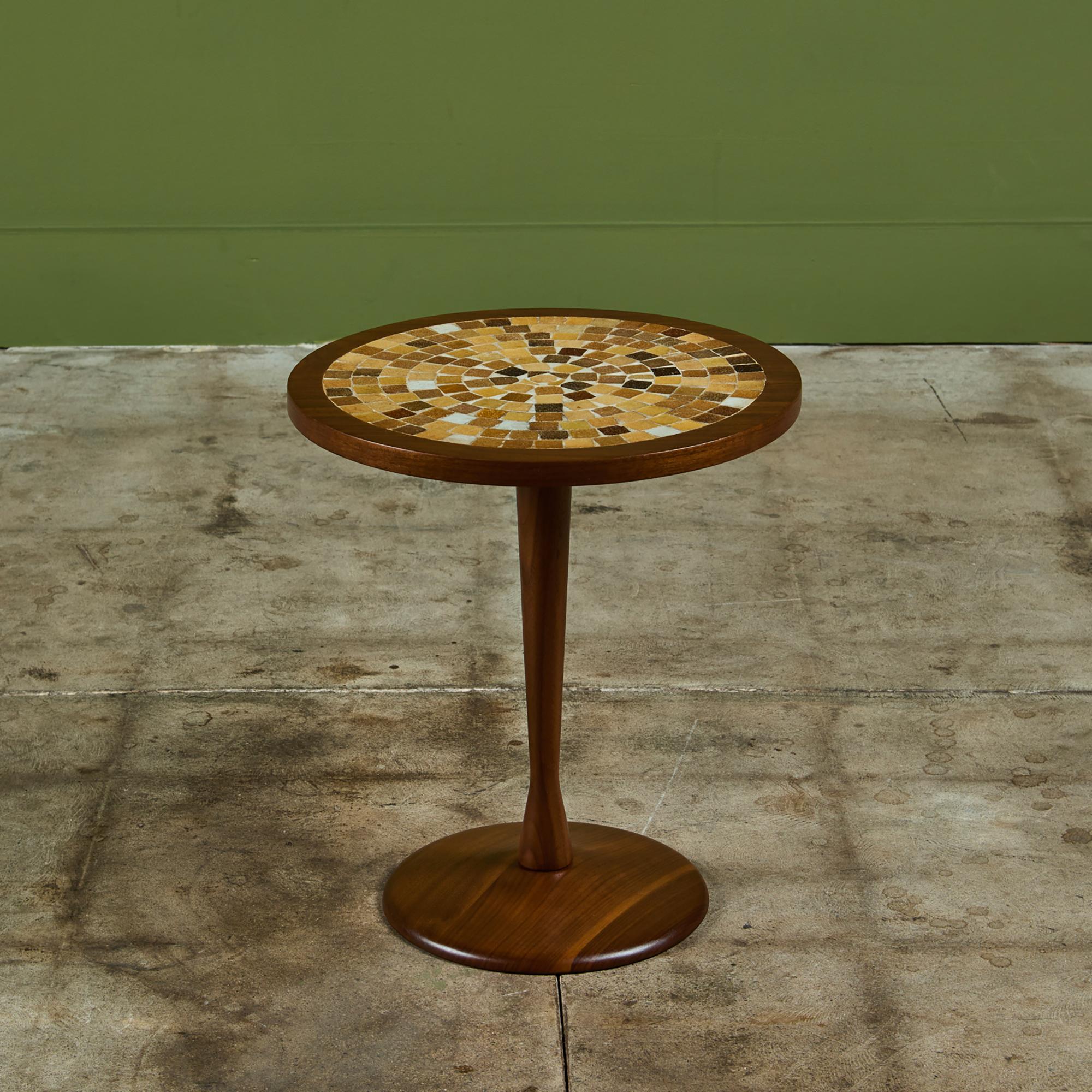 Mesa auxiliar redonda al estilo de Gordon & Jane Martz. El tablero de la mesa tiene incrustaciones de azulejos de cerámica con motivos geométricos. Los azulejos son tonos caramelo y caramelo de mantequilla. El armazón, la base y el pedestal de la
