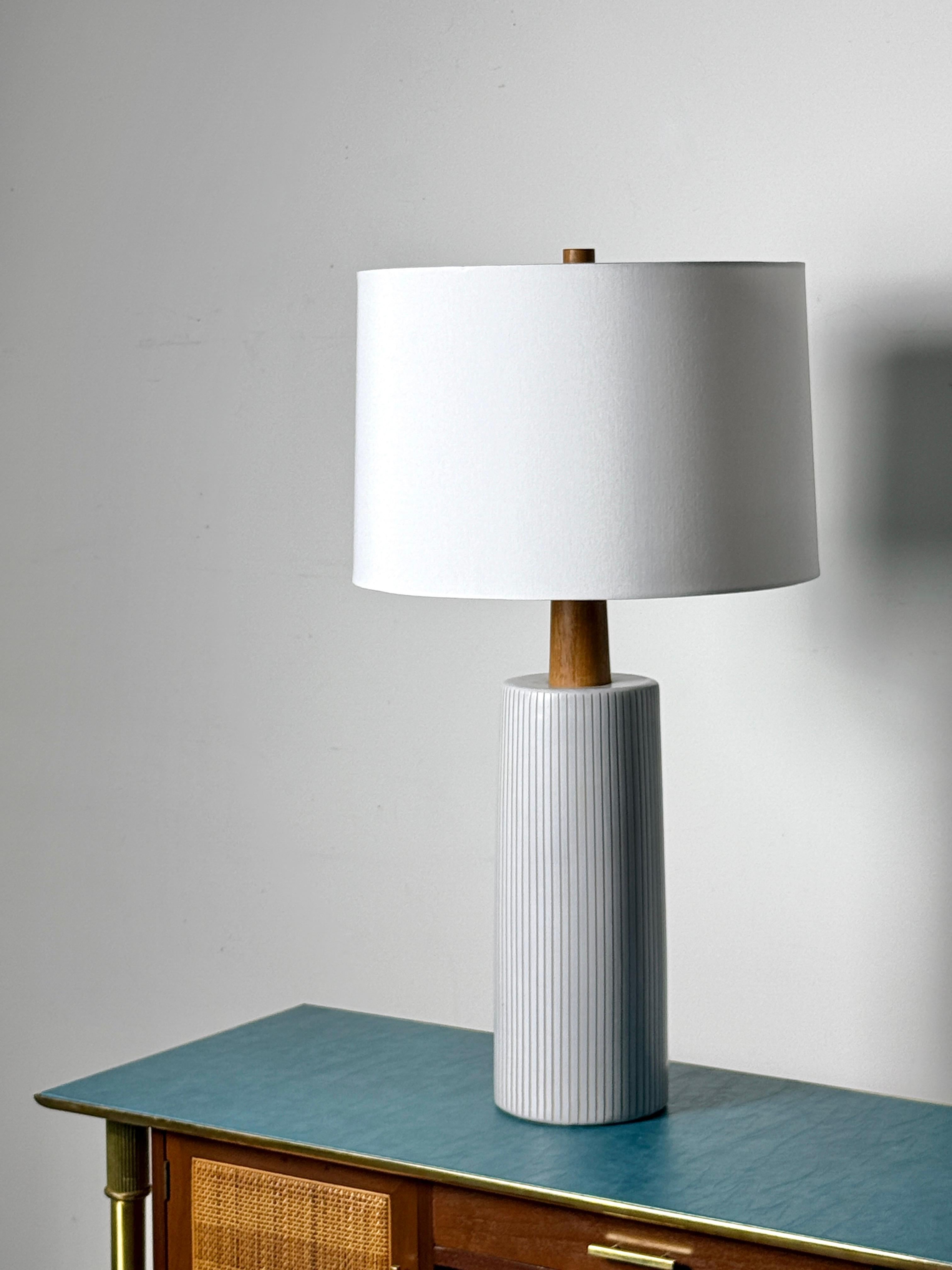 Mid Century stoneware ceramic table lamp designed by Gordon and Jane Martz for Marshall Studios circa 1960s

Model 191 in matte white glaze with vertical incised pinstripe design
Sculpted teak neck and finial with new drum shade

33 inch overall