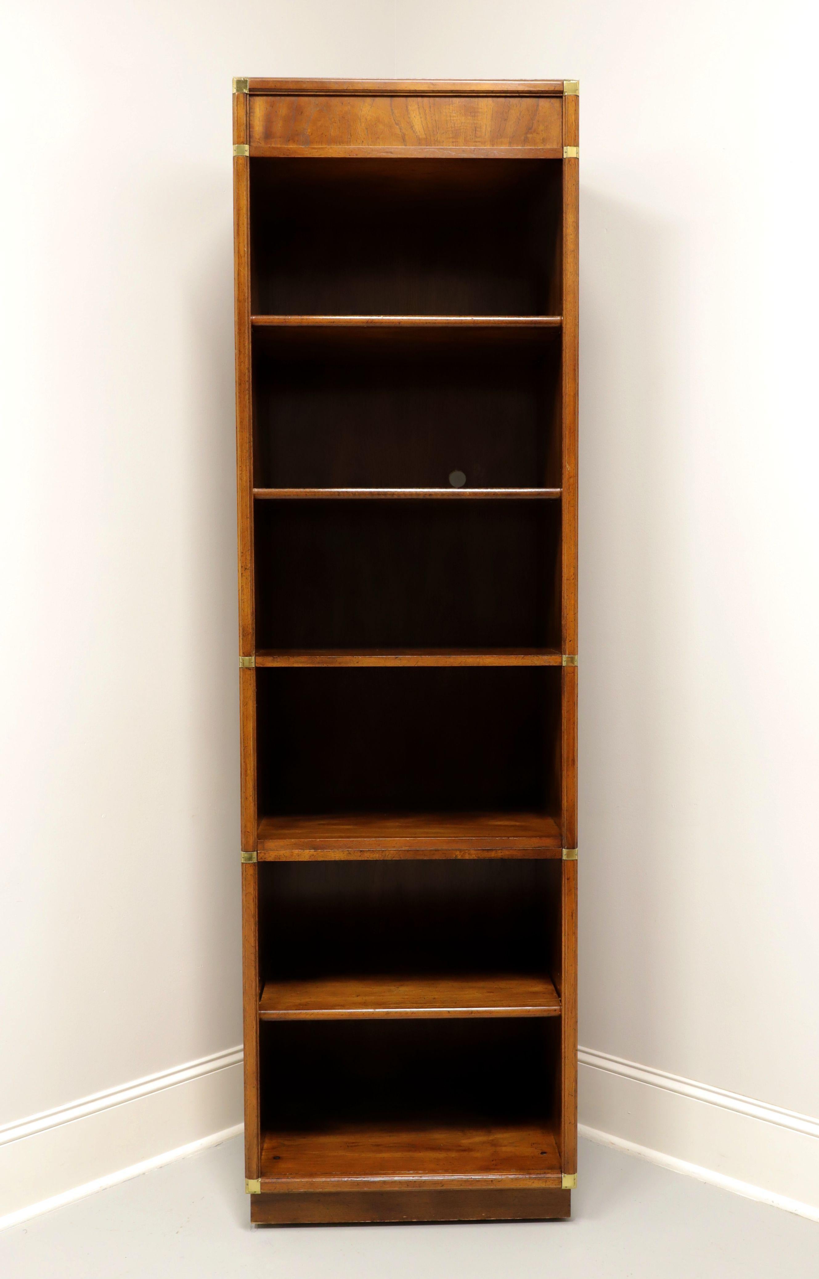 A Campaign style narrow shelving unit by Gordon's Furniture, of Johnson City, Tennessee, USA. Fruitwood with decorative brass accents. Features a flat front, double fixed shelf to center creating the appearance of an upper and lower section, one