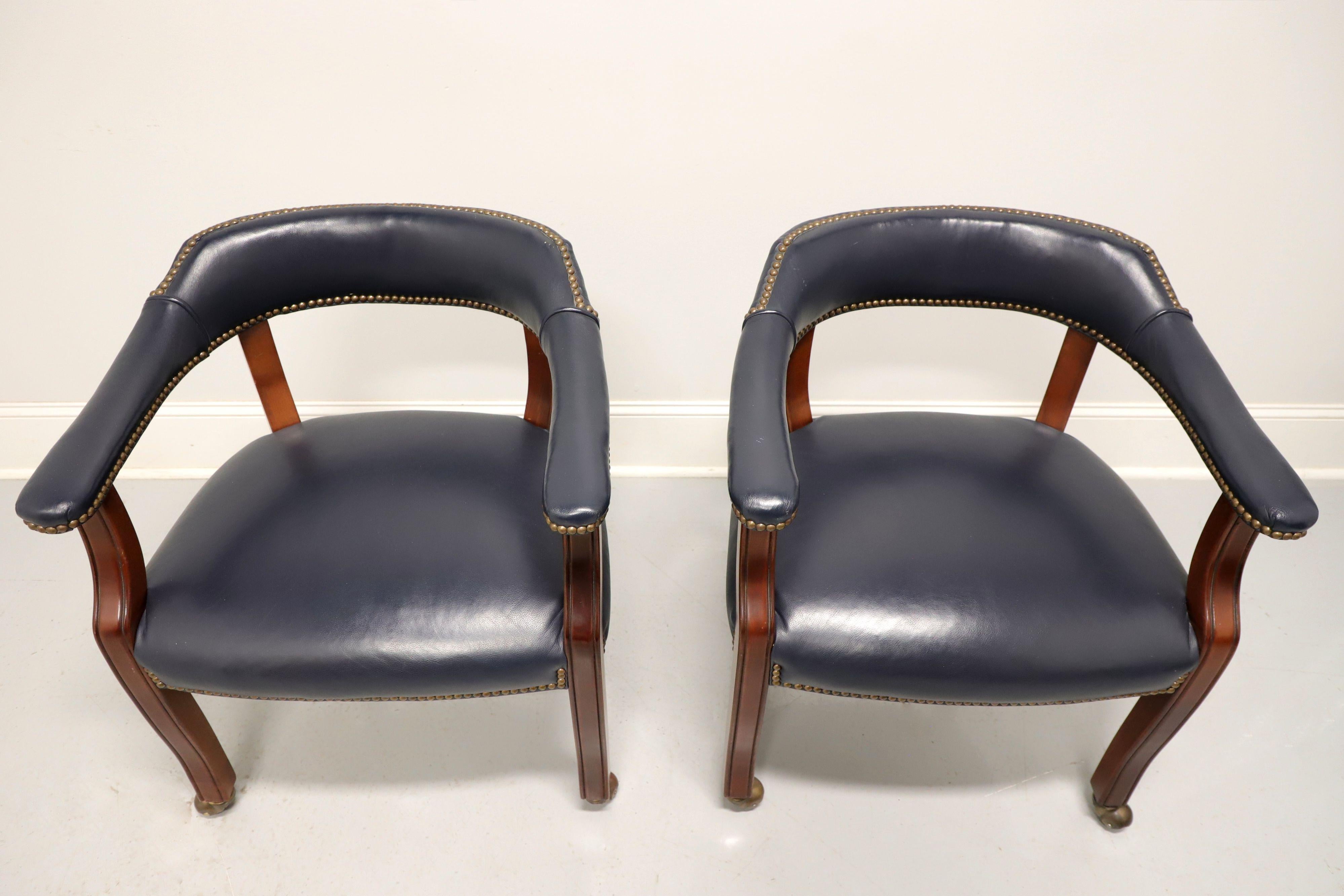 A pair of Traditional style game / club chairs on casters by Gordon's Furniture, of Johnson City, Tennessee, USA. Fruitwood frame with gray blue color leather upholstery, barrel back, brass nailhead trim, flared rear legs and straight front legs on