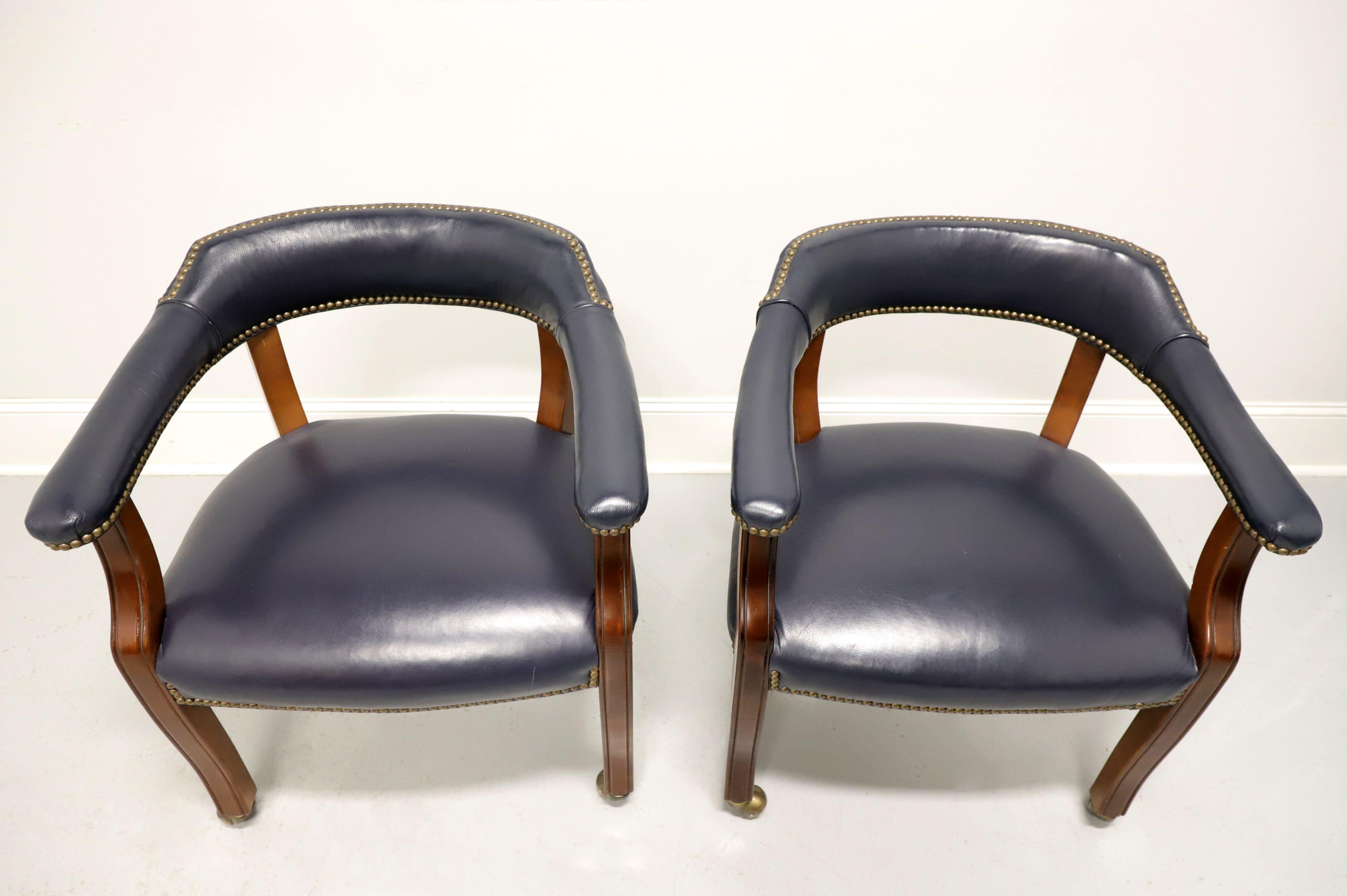 A pair of Traditional style game / club chairs on casters by Gordon's Furniture, of Johnson City, Tennessee, USA. Fruitwood frame with gray blue color leather upholstery, barrel back, brass nailhead trim, flared rear legs and straight front legs on