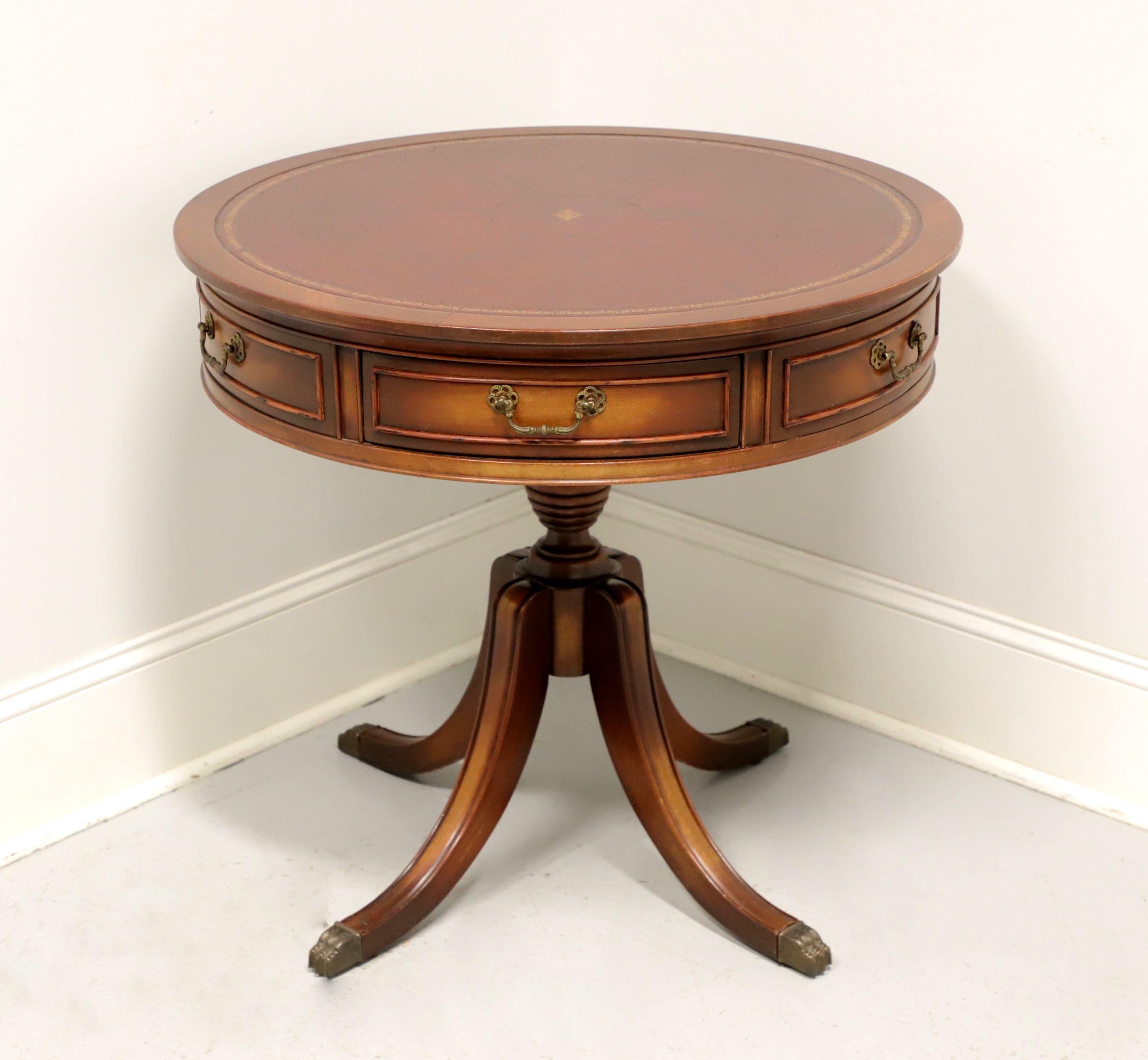 A Traditional style round drum table by Gordon's Furniture, of Johnson City, Tennessee, USA. Mahogany with banded & inlaid reddish-brown with gold band leather top, brass hardware, turned pedestal base and four legs with brass toe caps. Features two